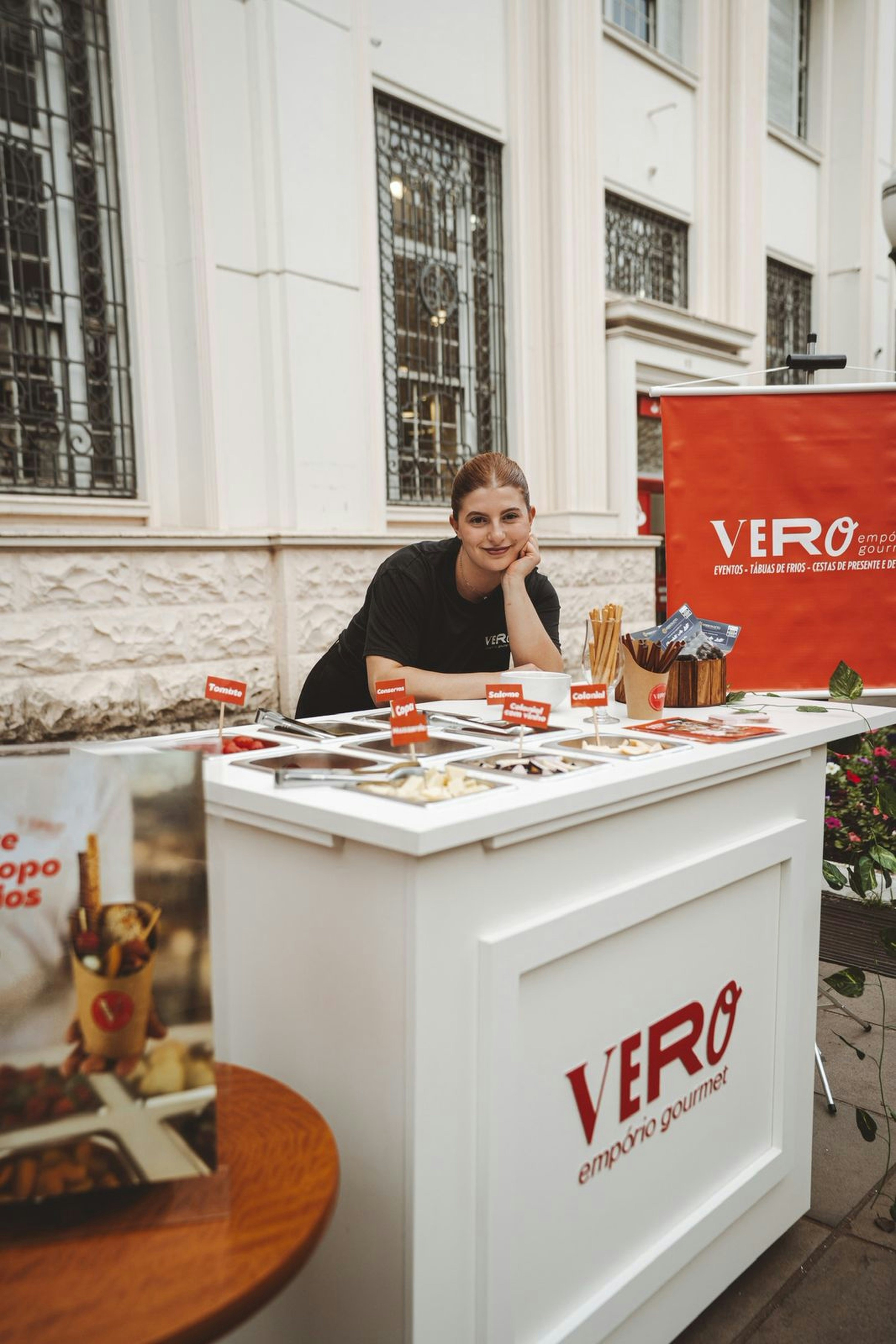 A smiling woman stands behind a food display table.