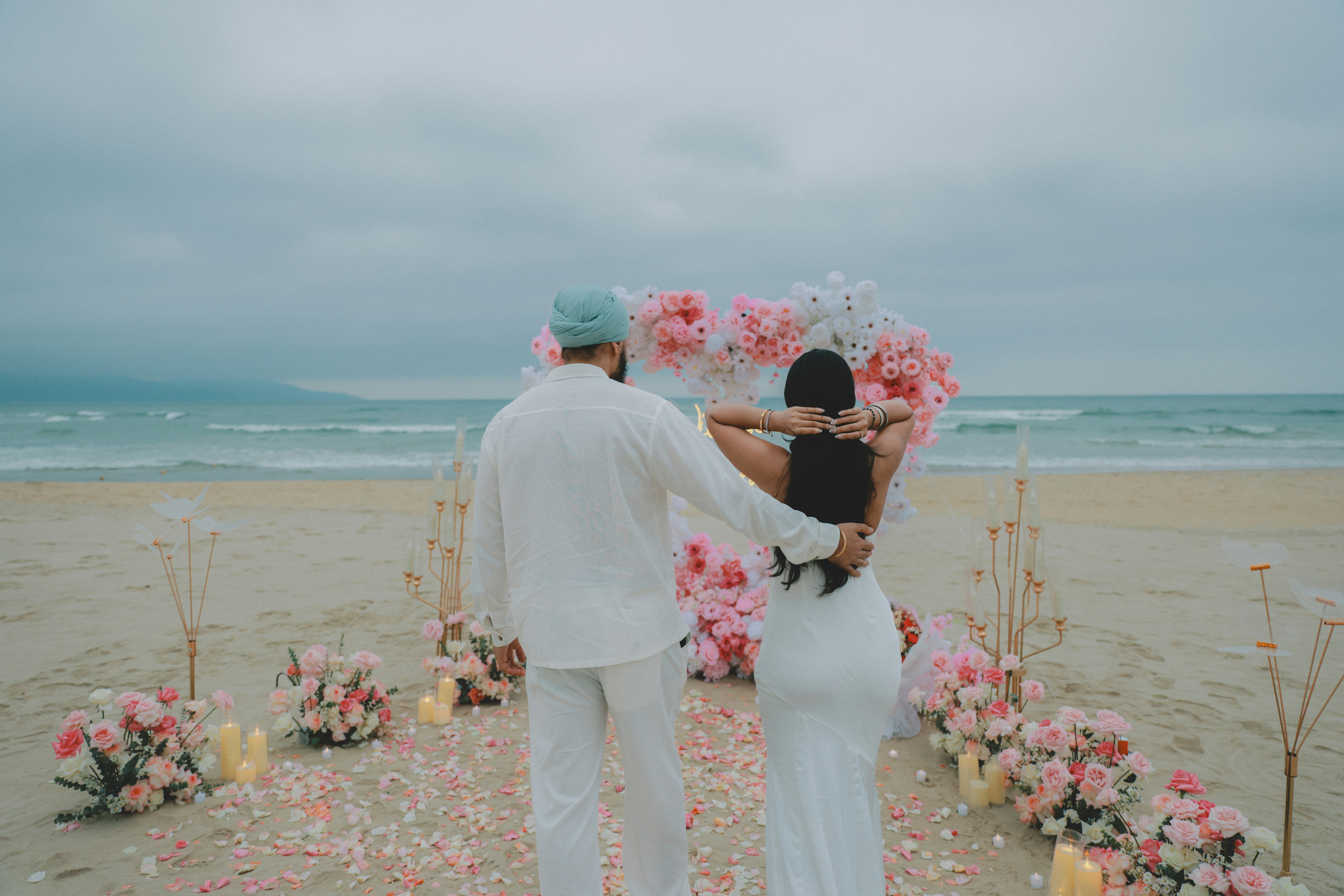 Un couple s’embrasse sur une plage avec une arche florale en forme de cœur.