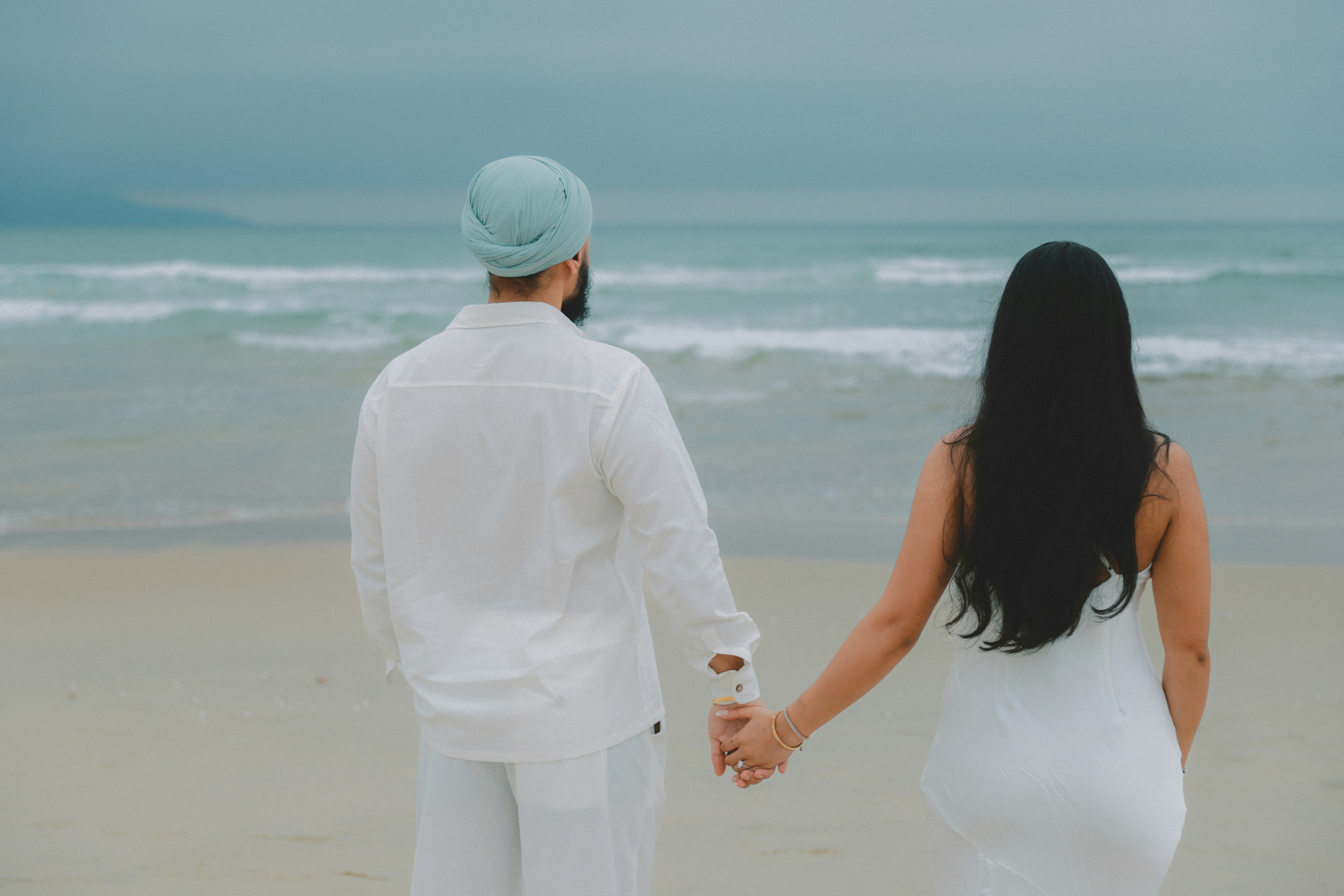 Couple se tenant la main sur une plage regardant l’océan
