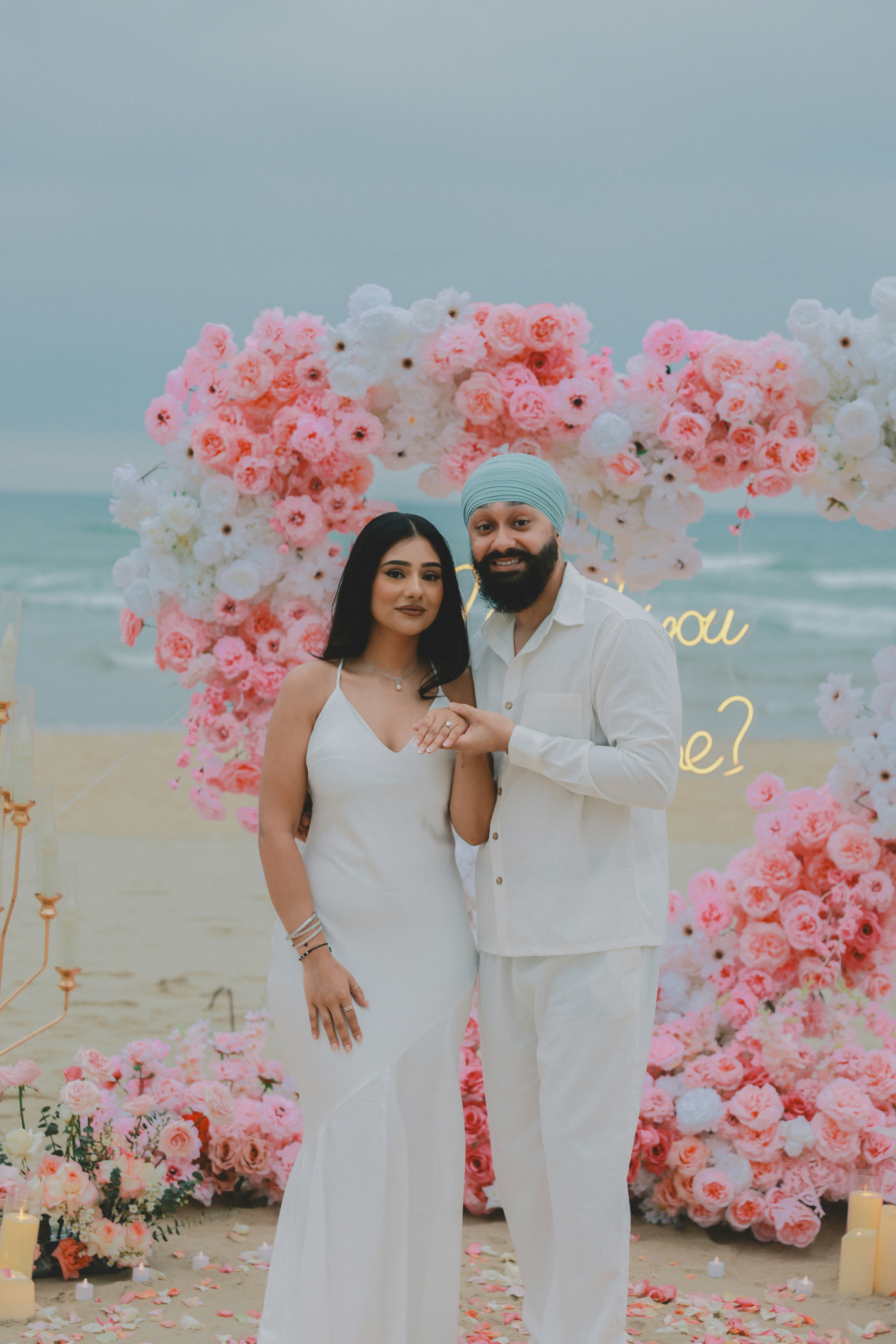 Couple posant sur une plage avec une arche en forme de cœur floral