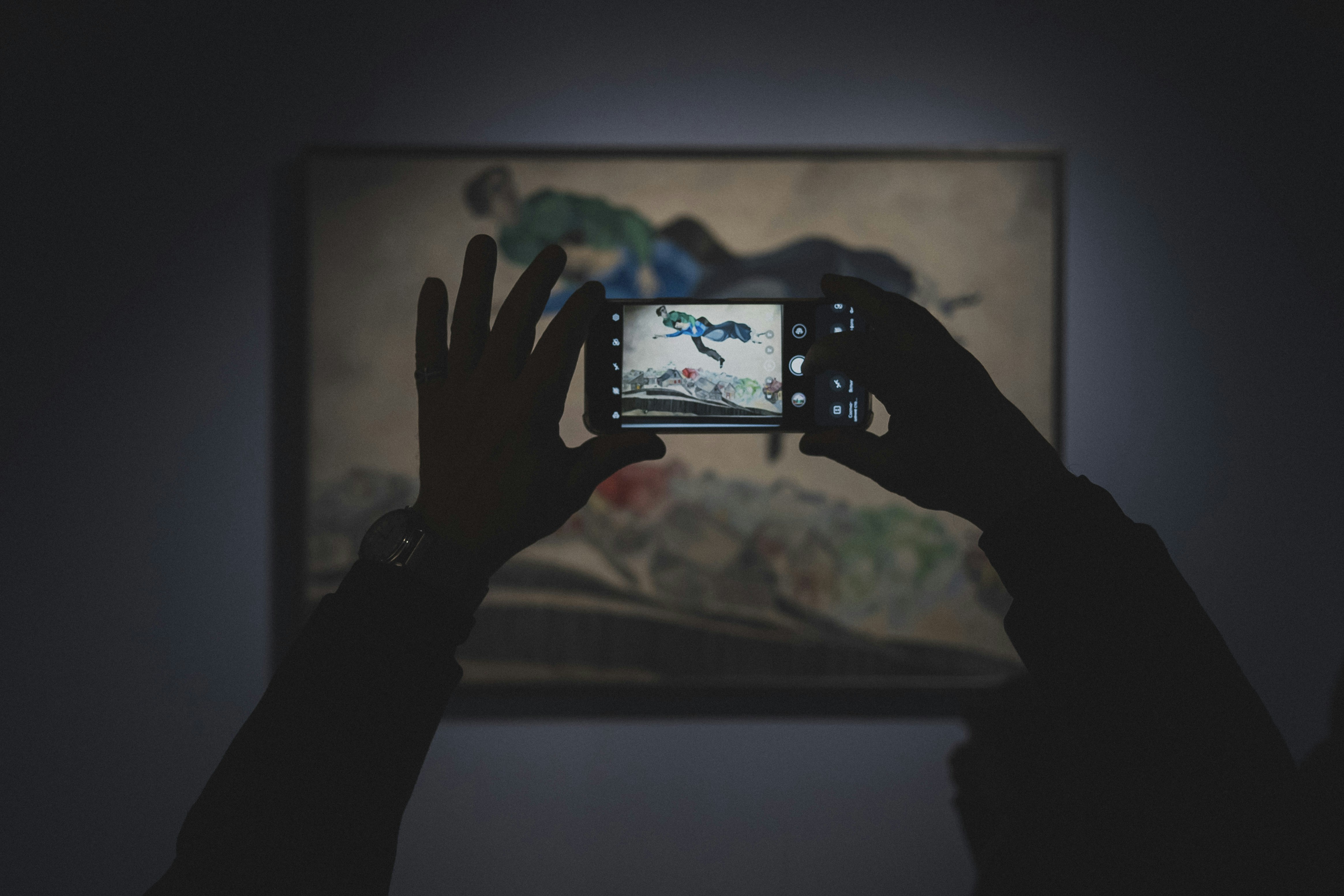 Hands holding camera photographing abstract painting