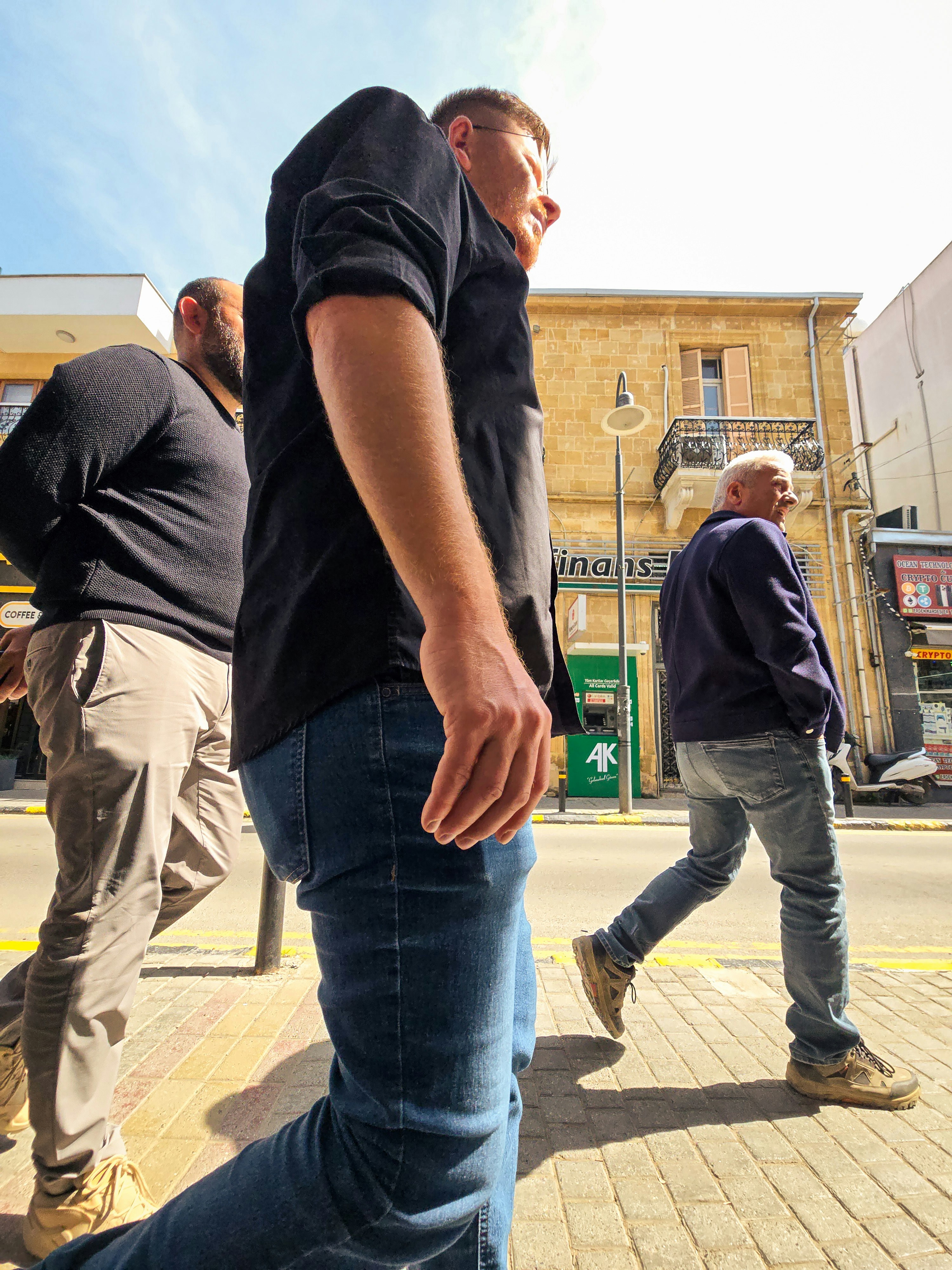 Three men walking down a sunny city street.