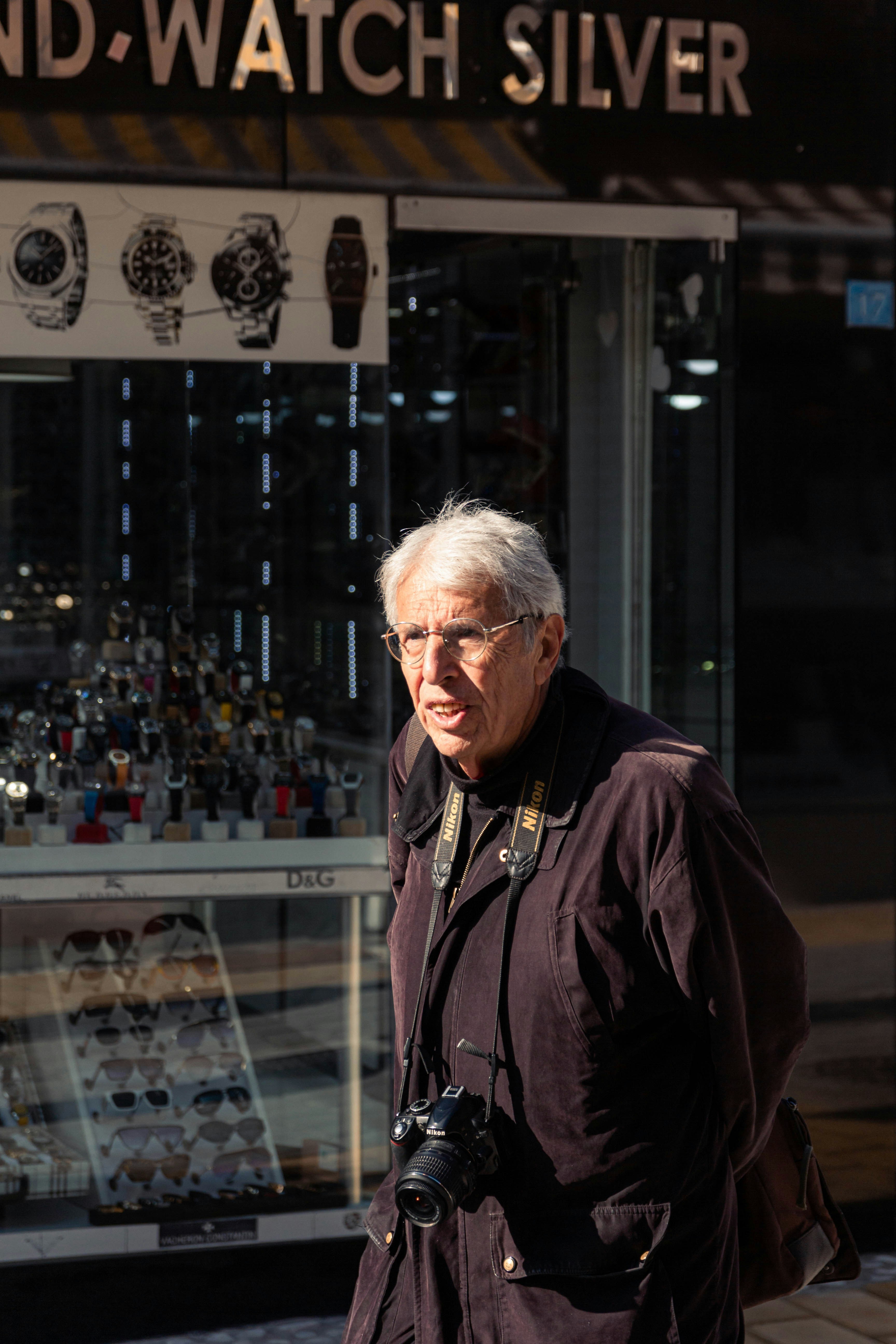 Elderly man with camera walks past watch store