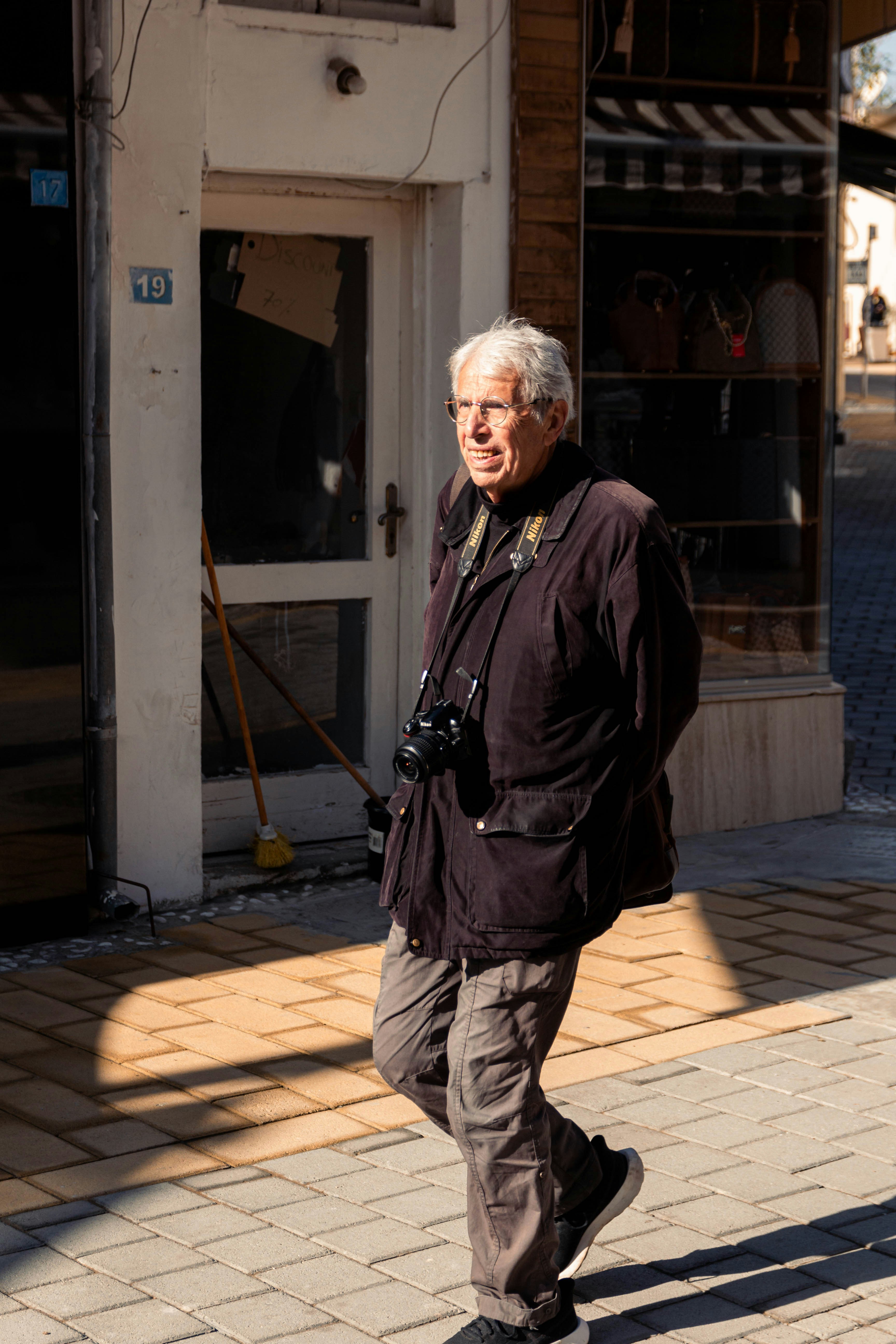An elderly man with a camera walks down a street.