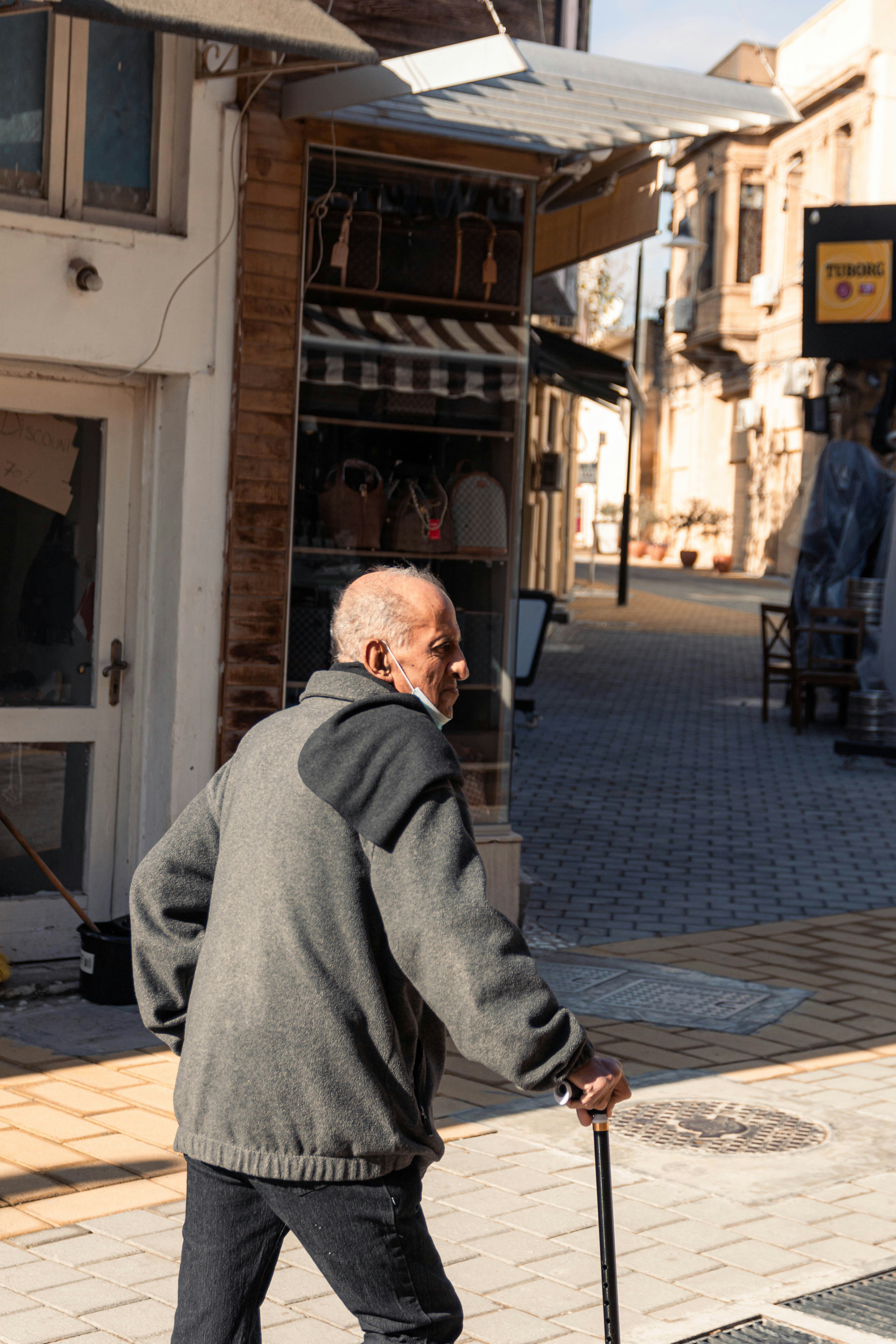Elderly man with cane walking down a street.