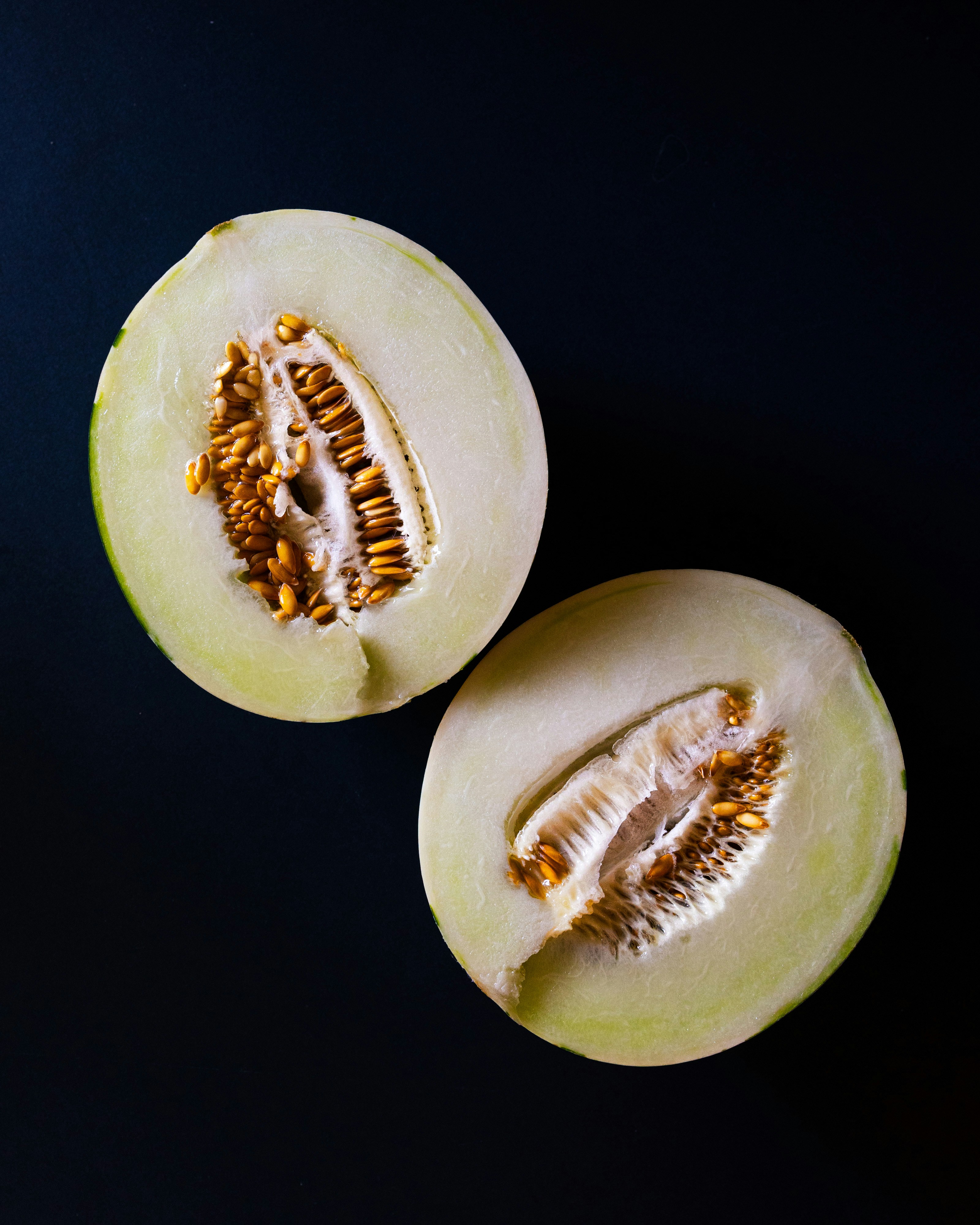 Two halves of a honeydew melon on a dark background