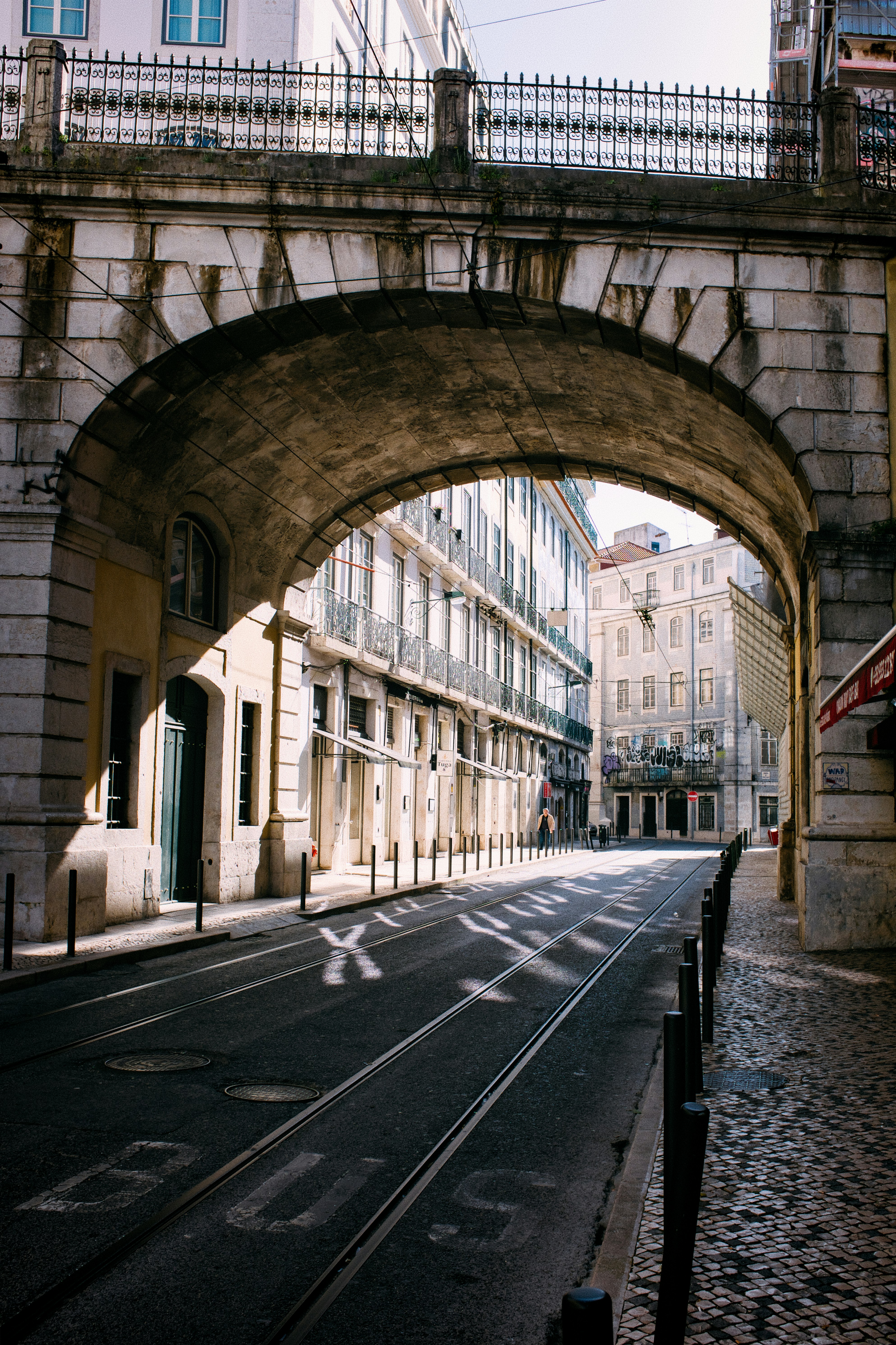 Stone archway over a street with tram tracks.