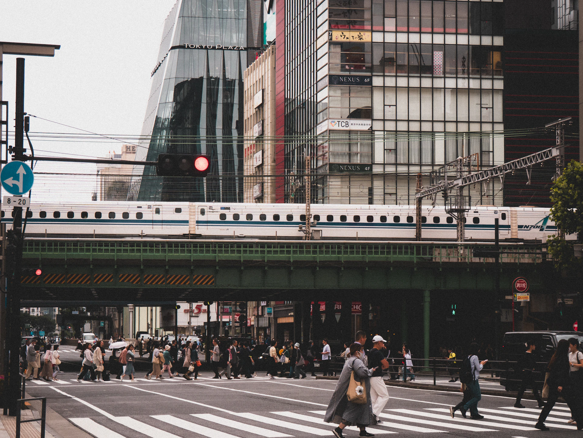 People crossing street under train tracks in city.