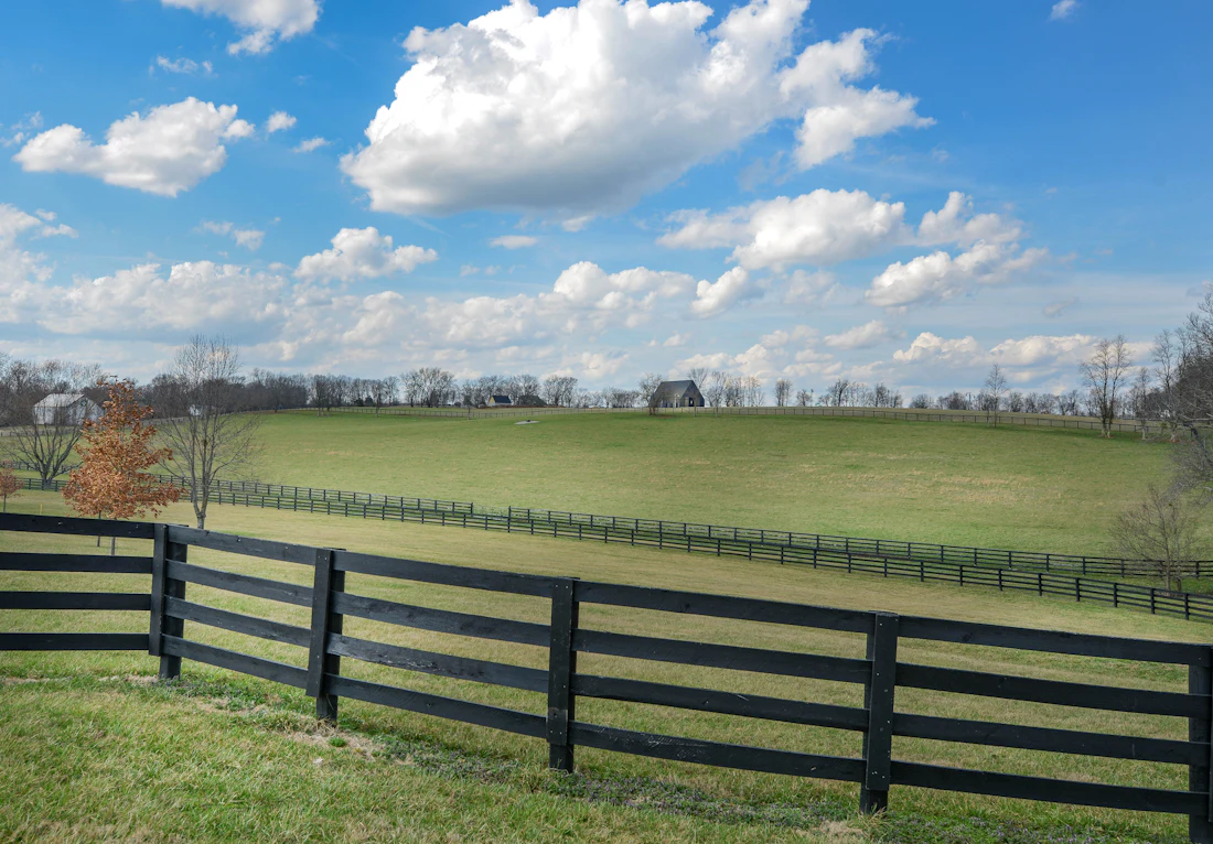 Black four-board ranch fence across a green pasture under blue sky
