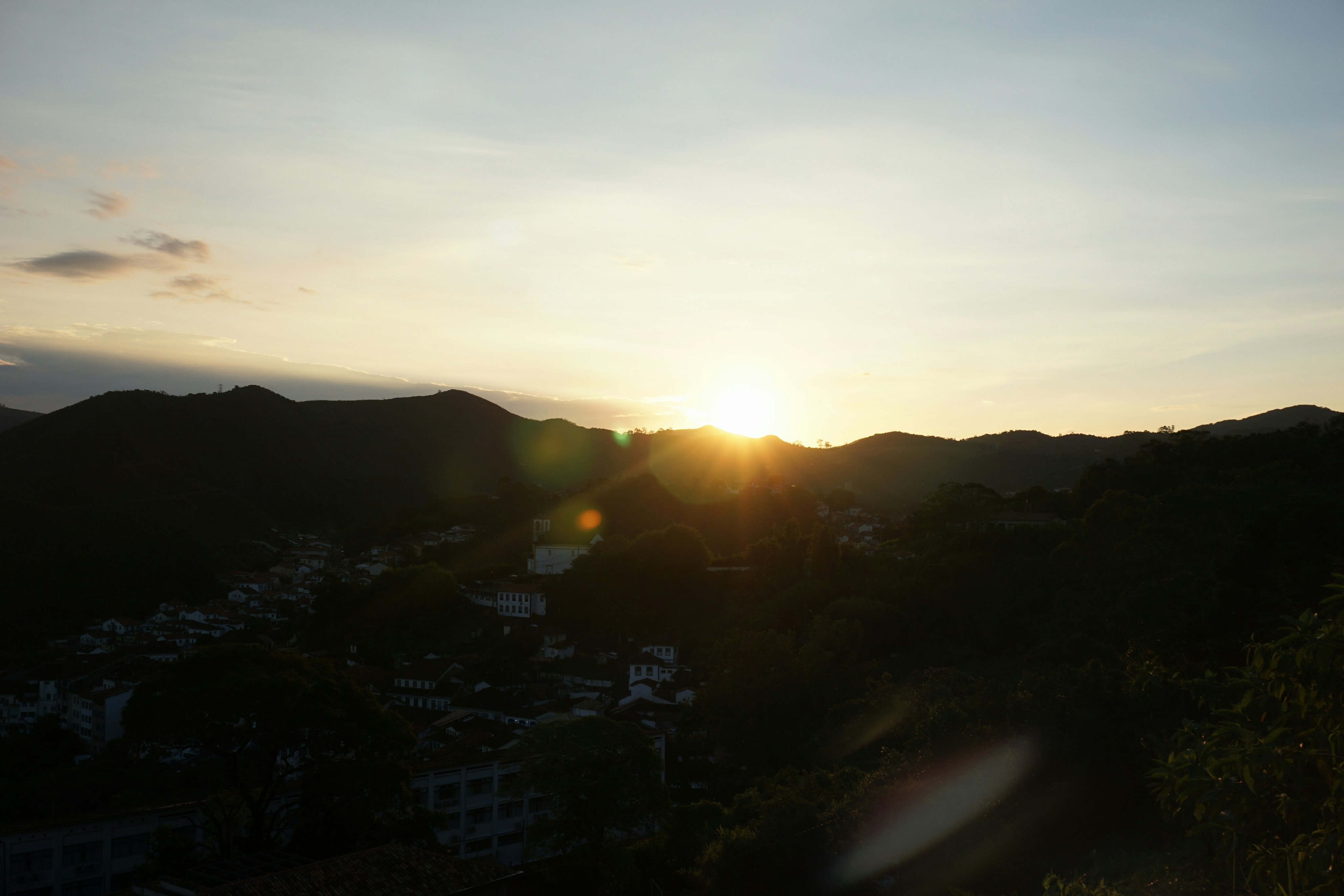 Puesta de sol sobre una cordillera y un pueblo en silueta.