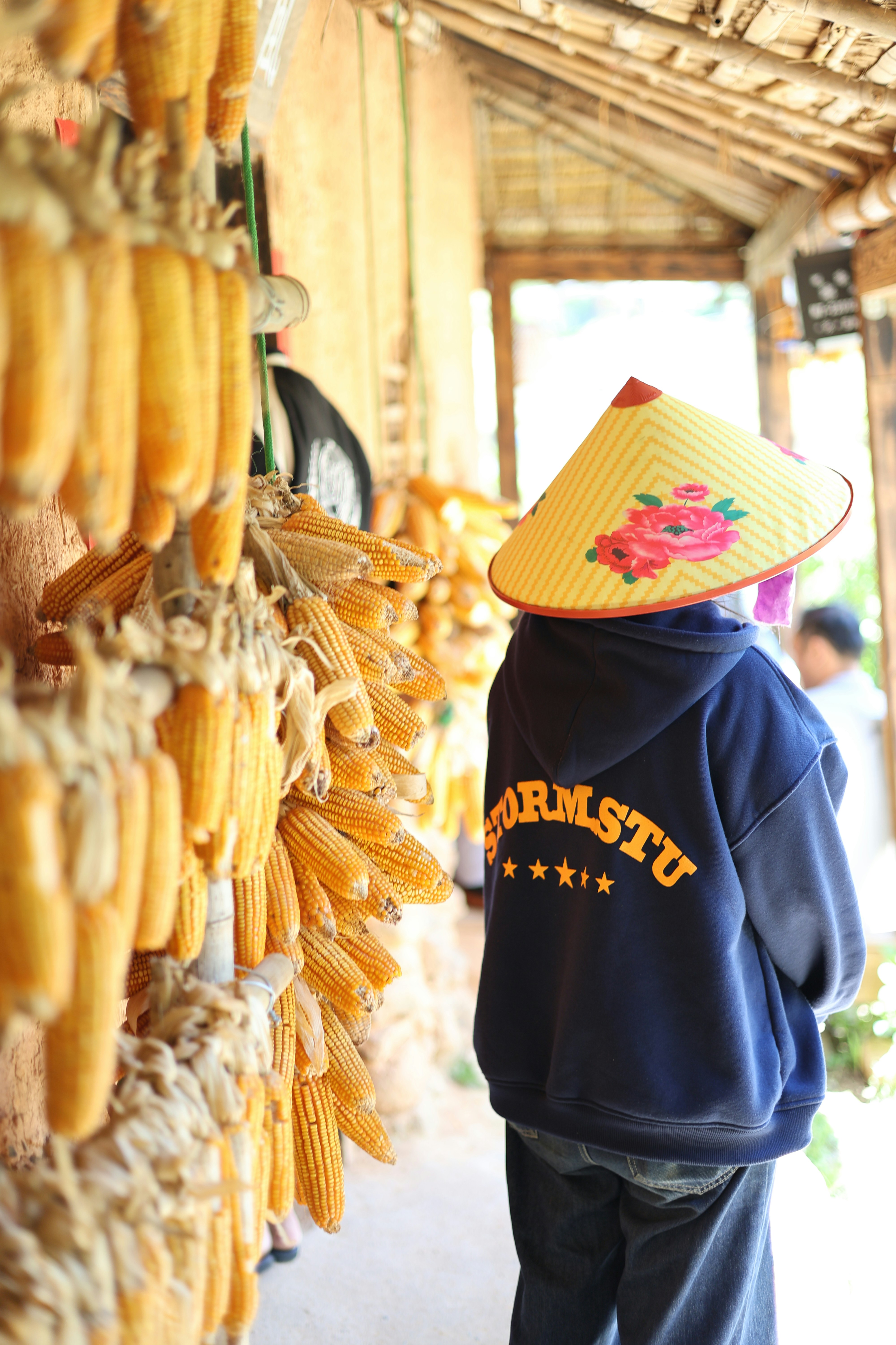Person in conical hat near drying corn cobs