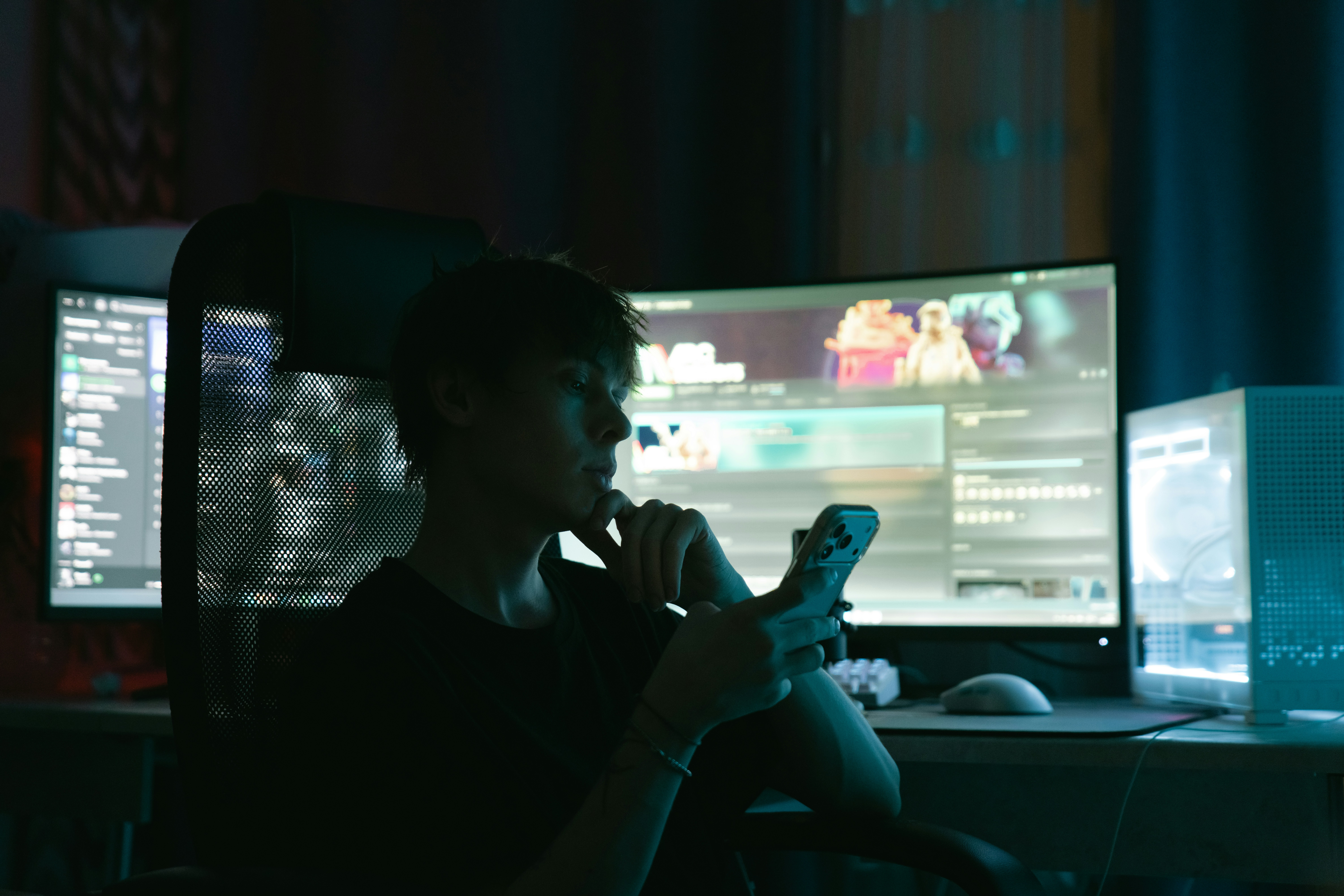 Person looking at phone in front of multiple computer monitors