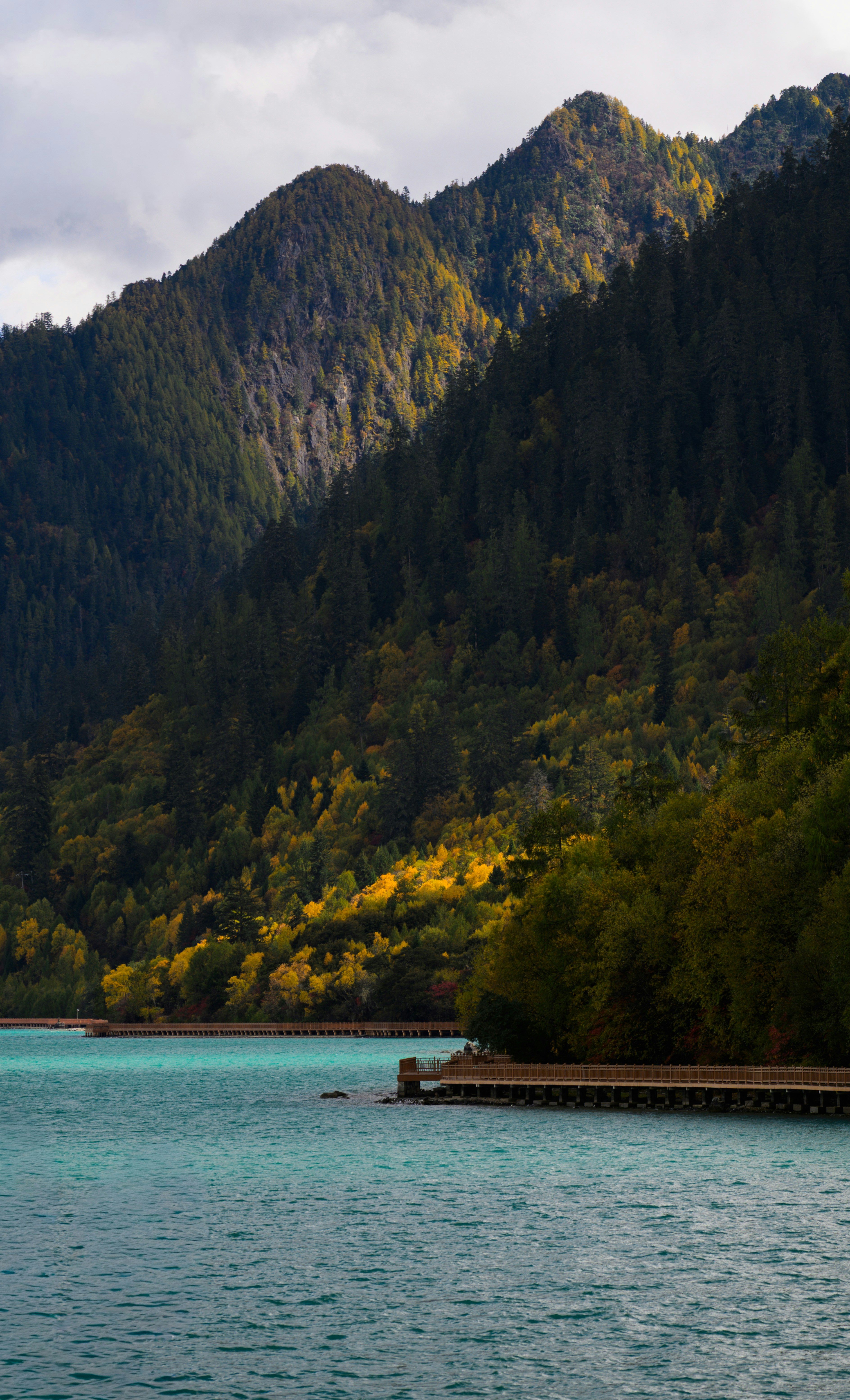 Turquoise lake with forested mountains and a pathway.