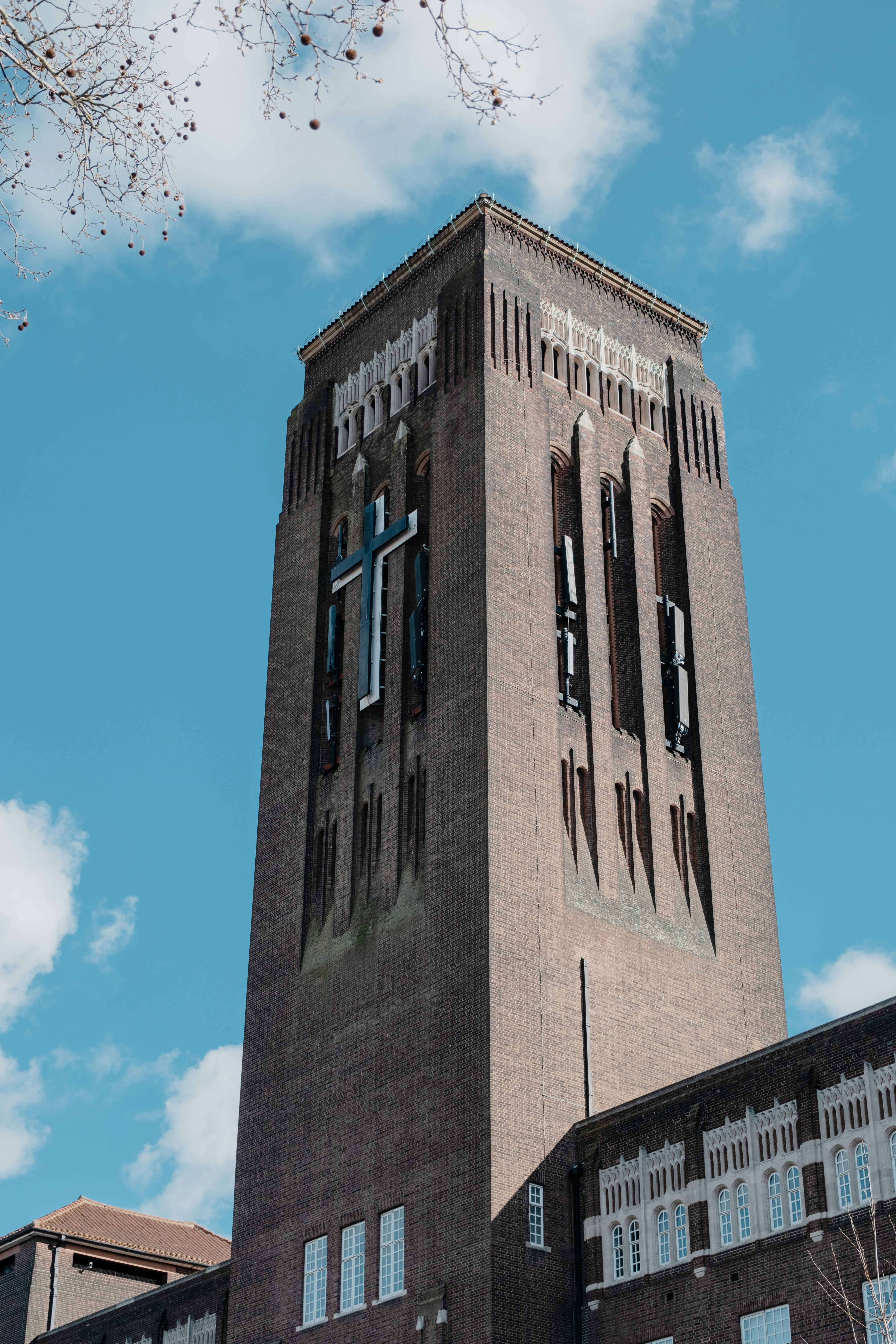 Torre alta de tijolos com uma grande cruz contra o céu azul.