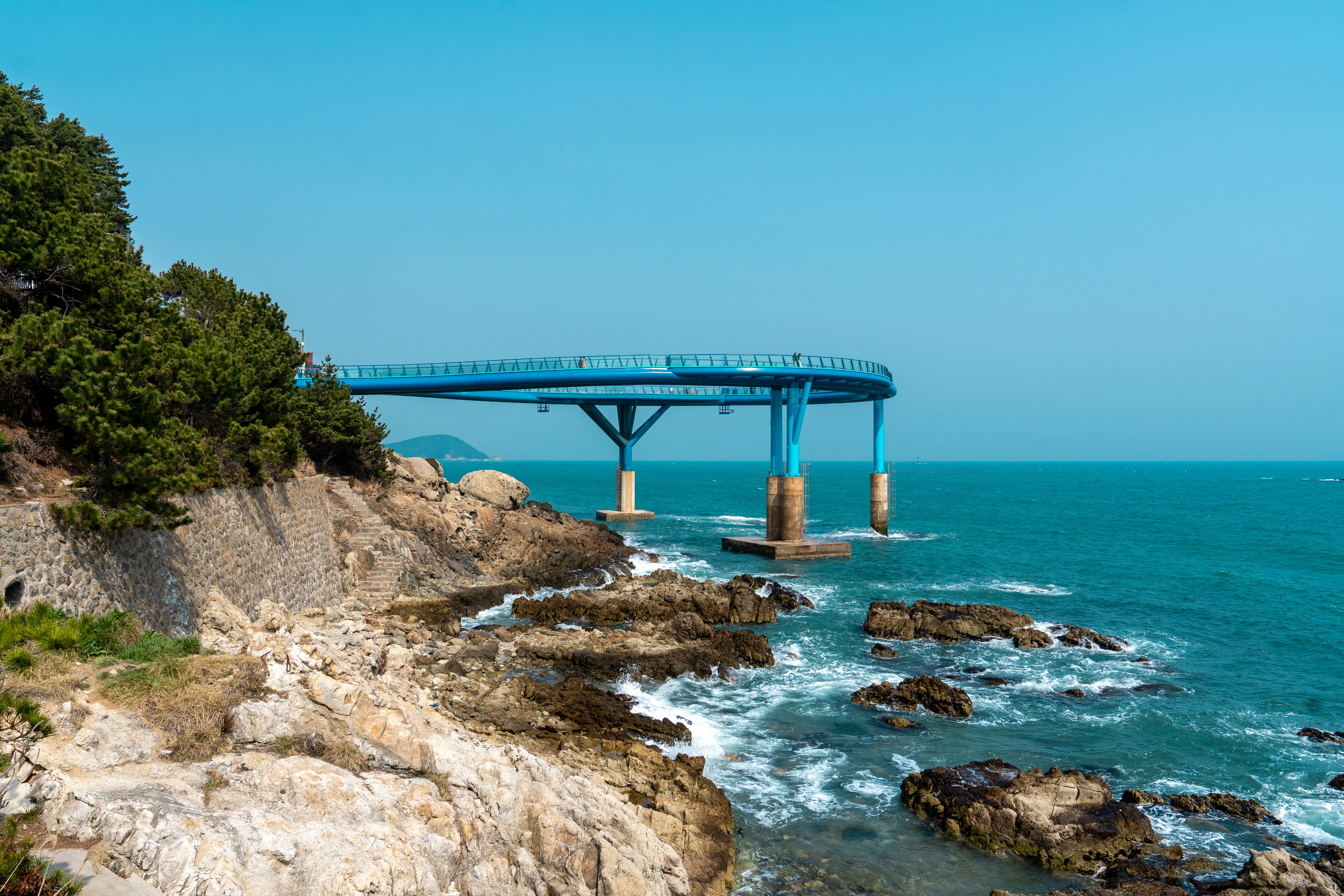 Cielo azzurro su una costa rocciosa con un ponte moderno.
