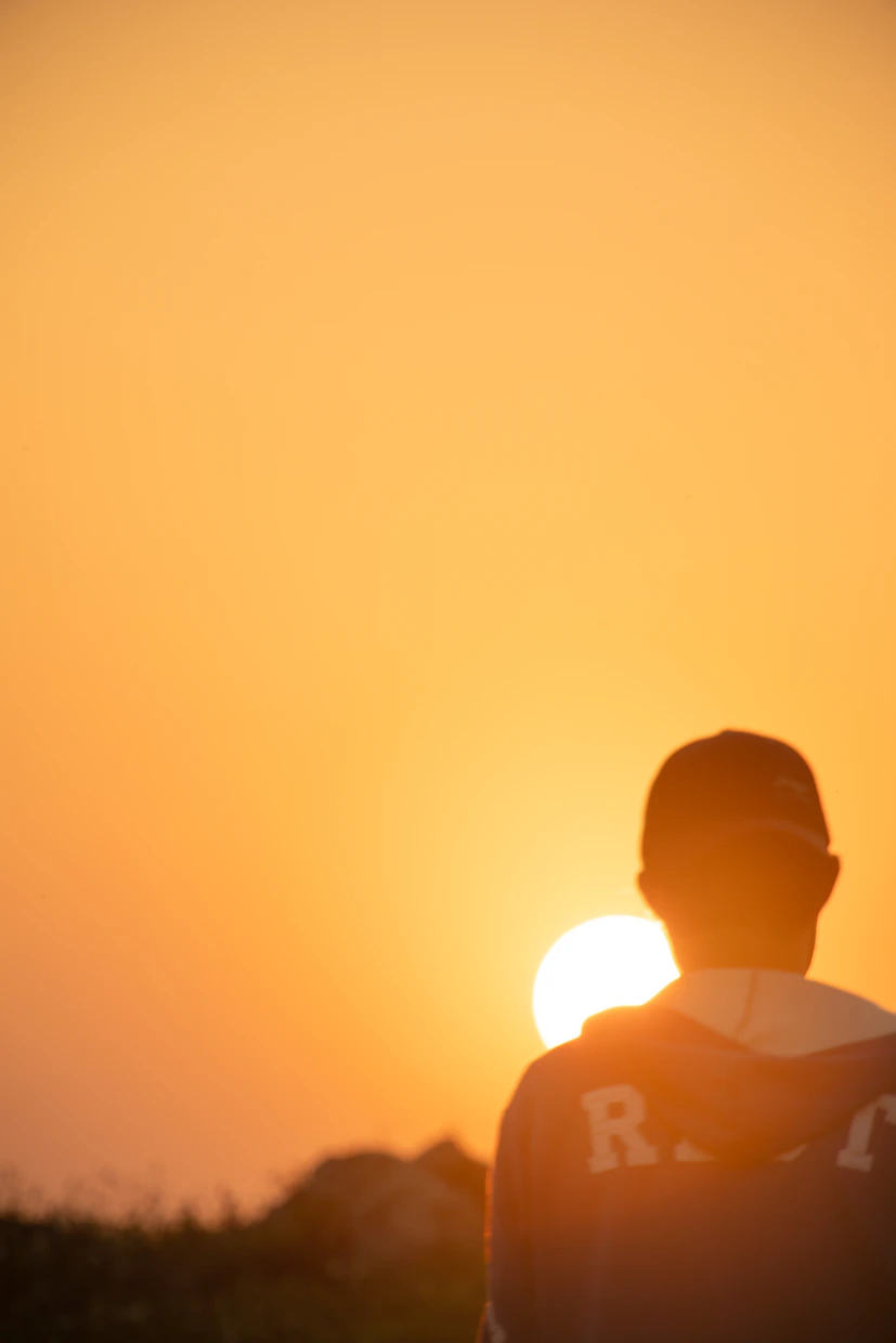 Une personne regarde le soleil se coucher à l'horizon.