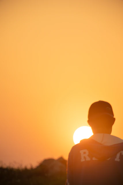 Une personne regarde le soleil se coucher à l'horizon.