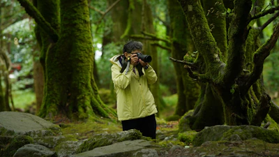 Person photographing in a mossy, green forest.