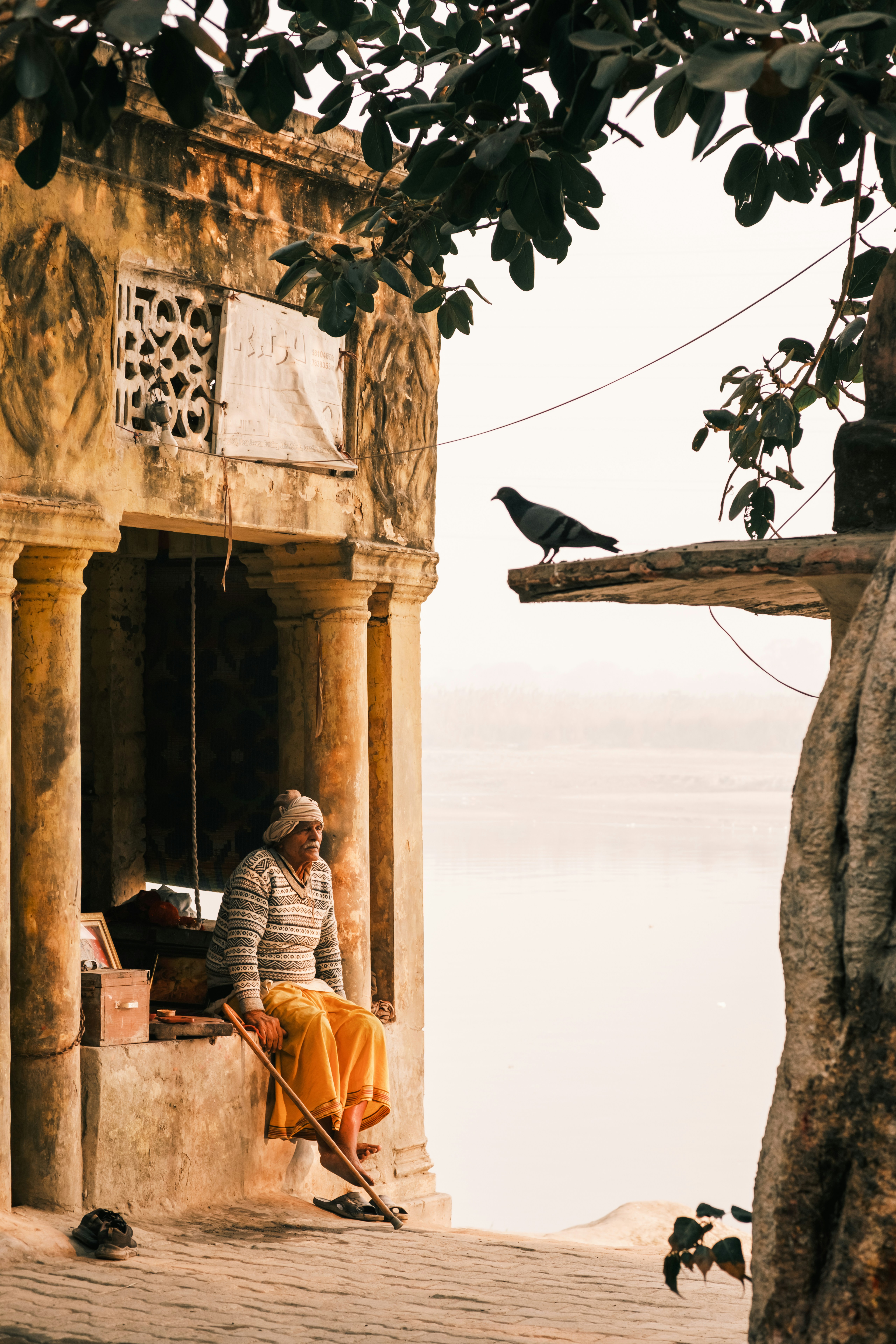 Elderly man sits near ancient building with pigeon perch