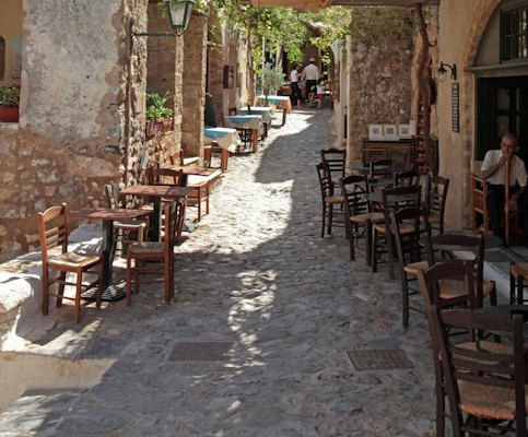 Outdoor cafe tables line a cobblestone street — Monemvasia, Greece