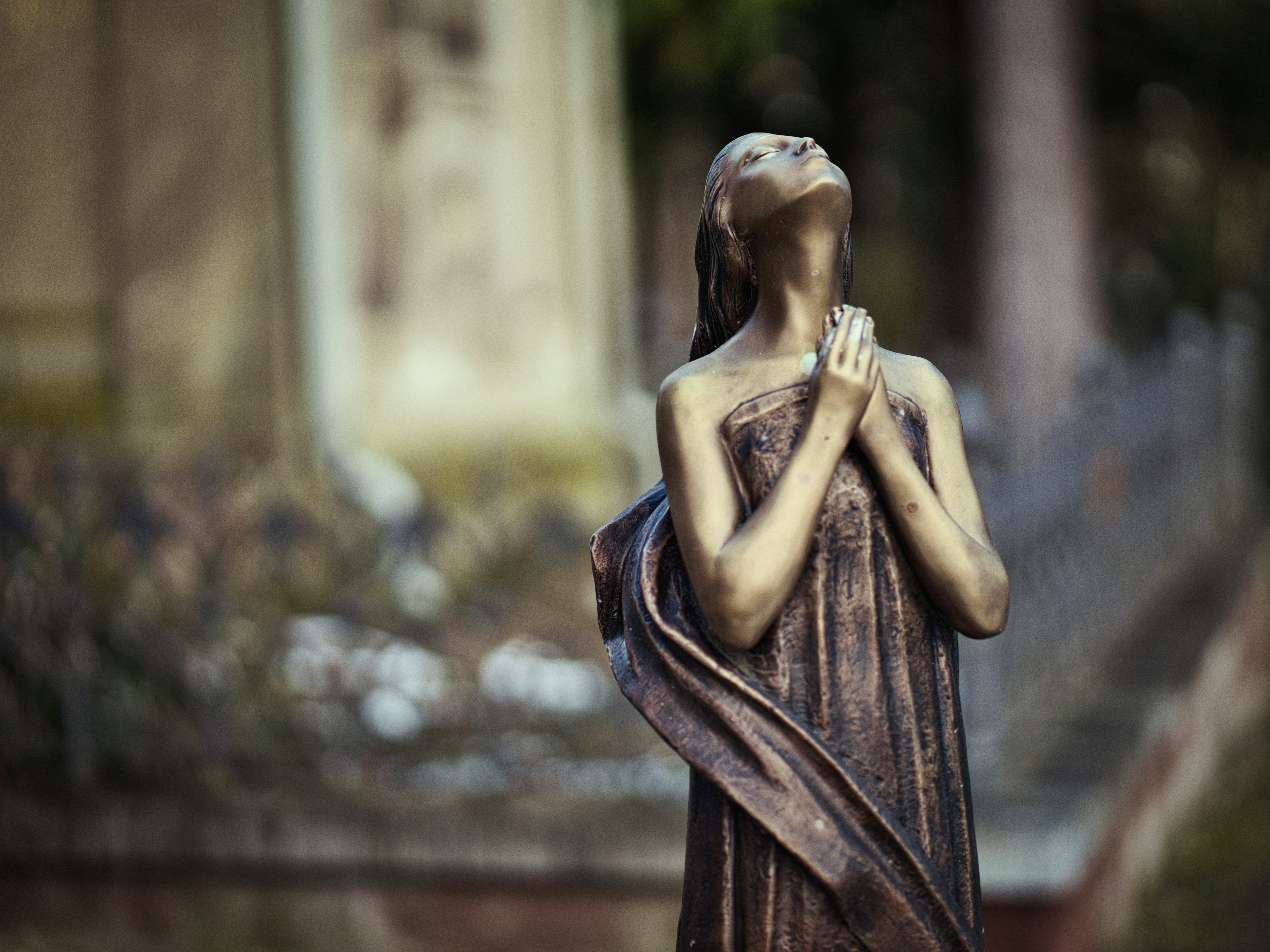 A bronze statue of a woman praying in a cemetery.