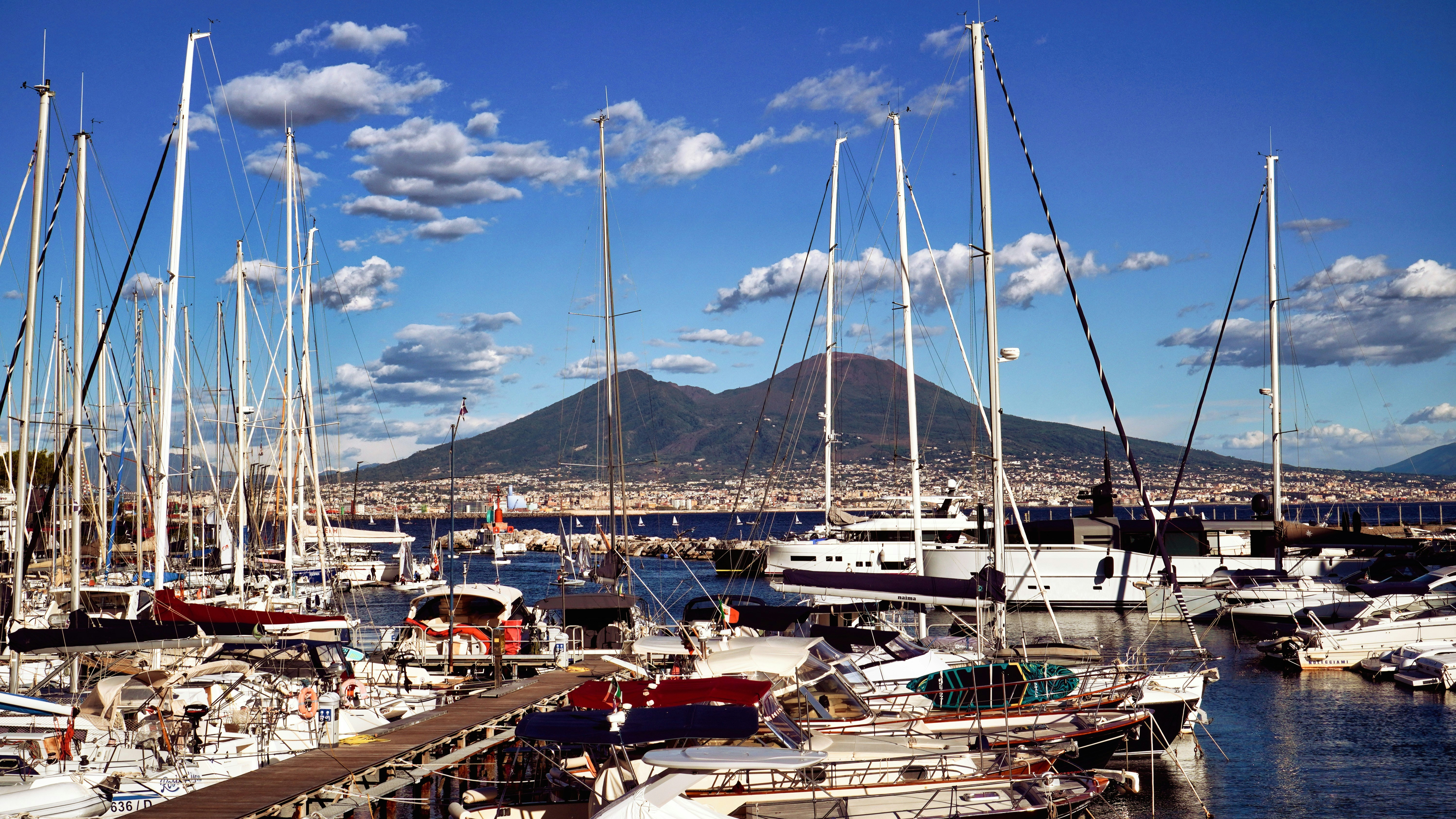 Sailboats docked in a harbor with a mountain backdrop.