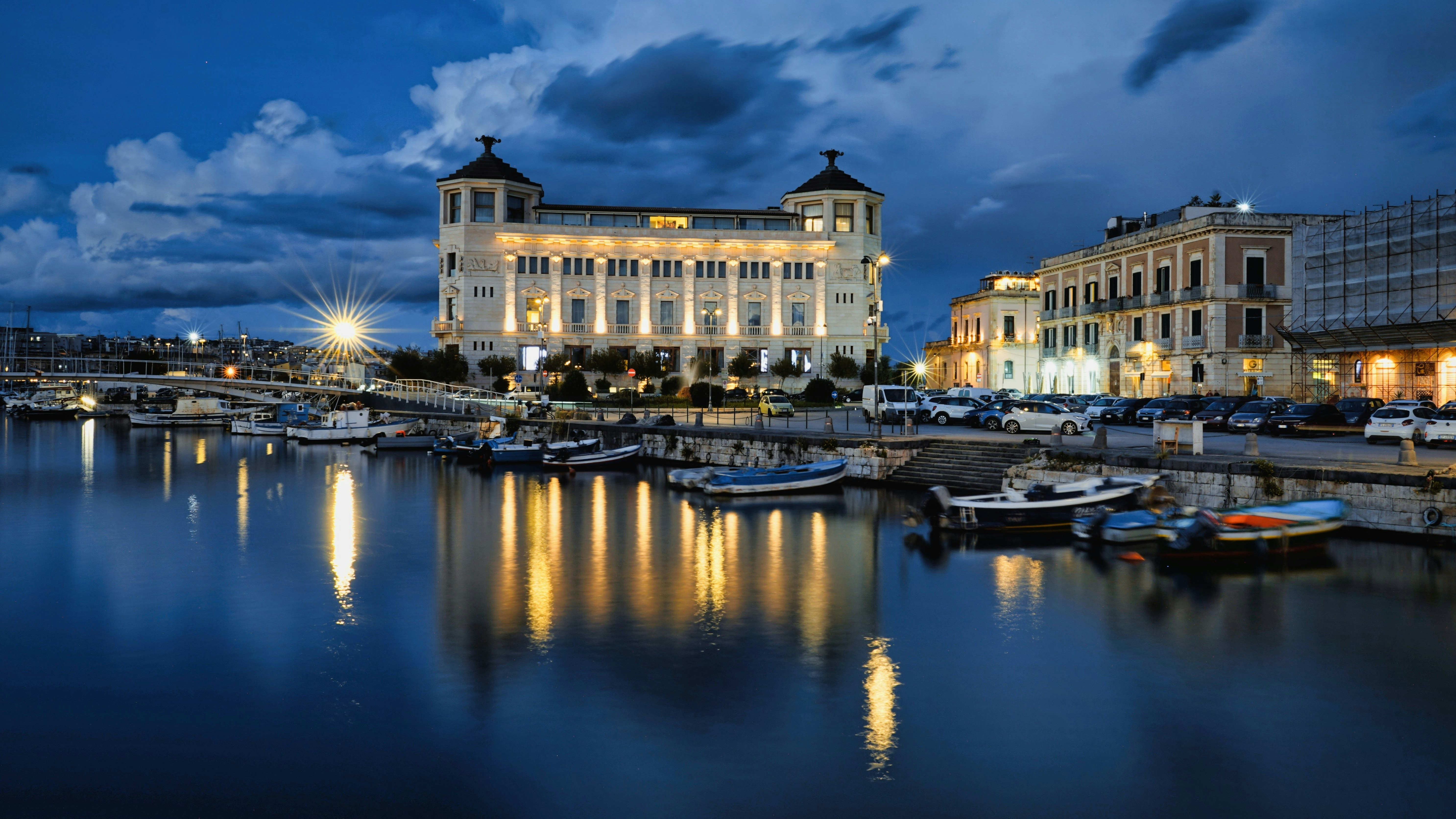Boats docked in a harbor with illuminated buildings at night.