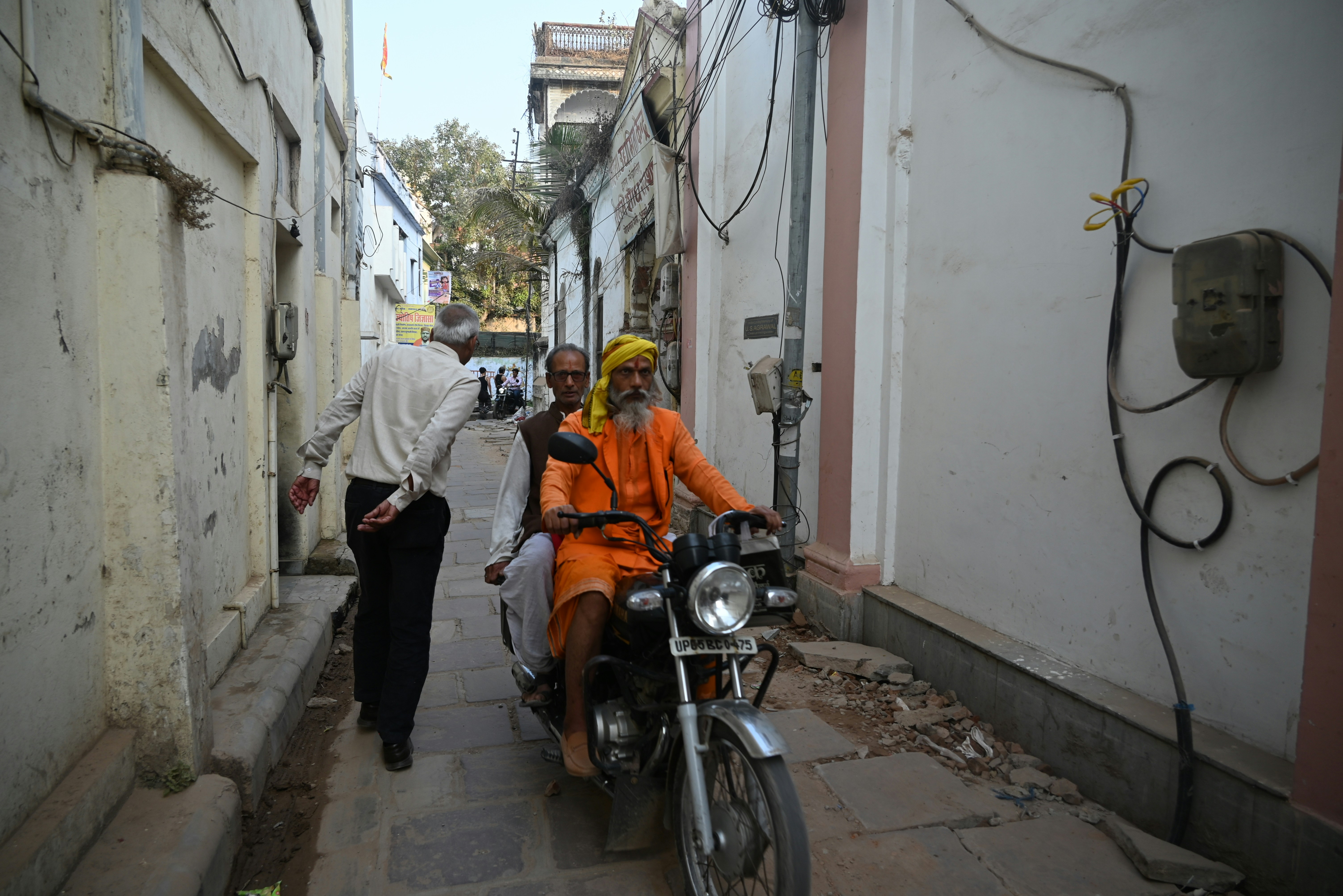 two men ride a motorcycle down a narrow alley