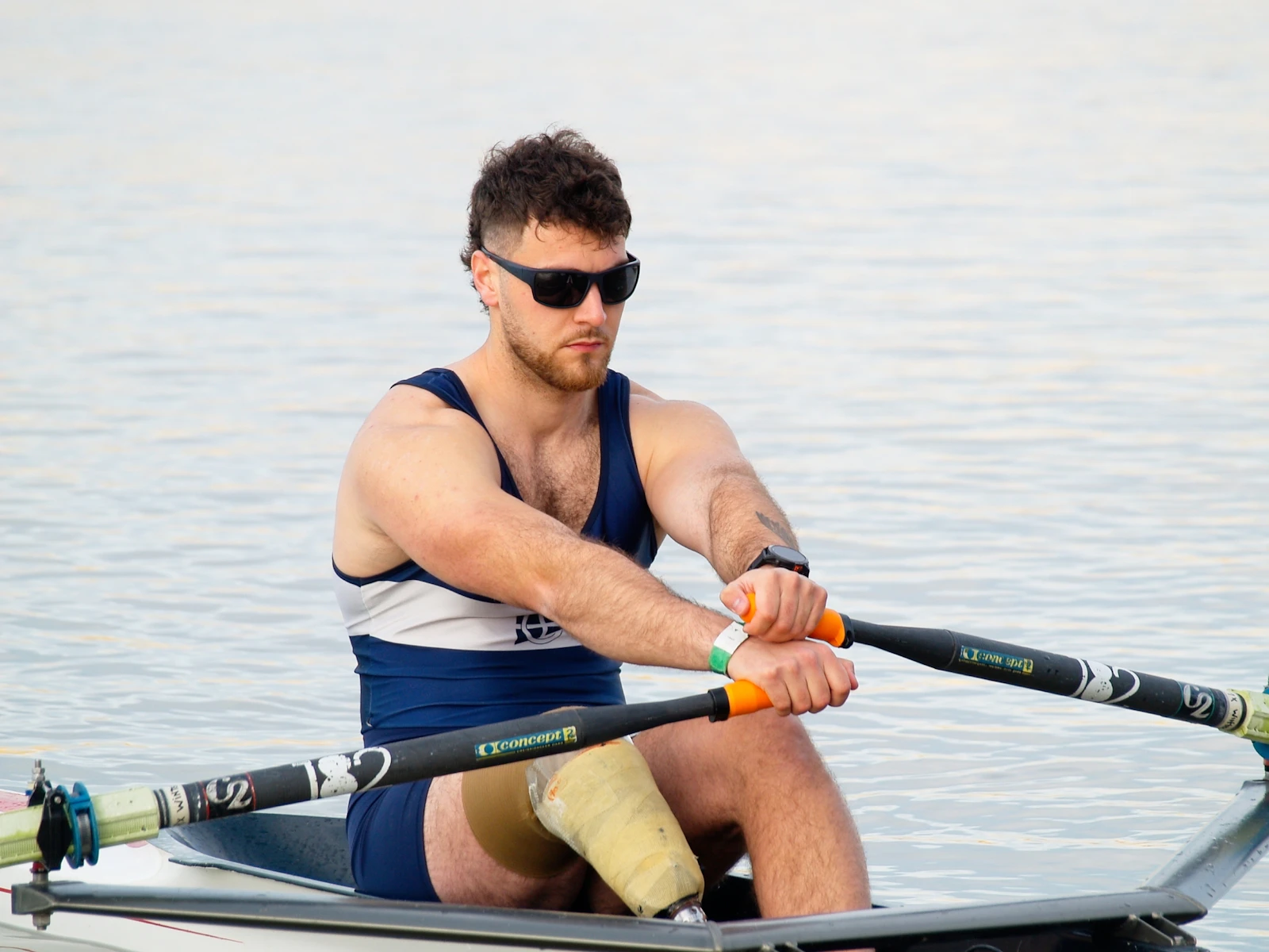 Rower carrying a single scull beside the river