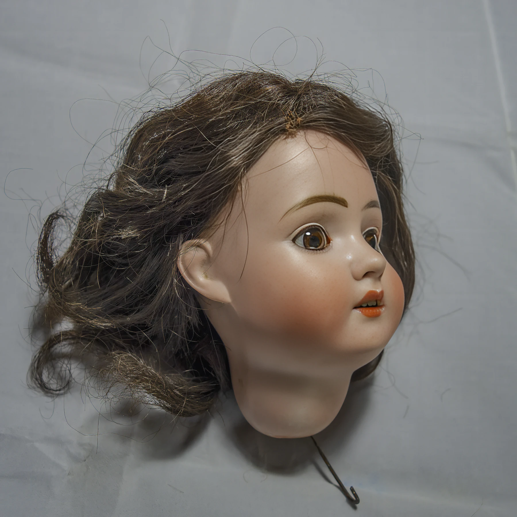 An antique bisque doll head with a brown wig lying on pale cloth