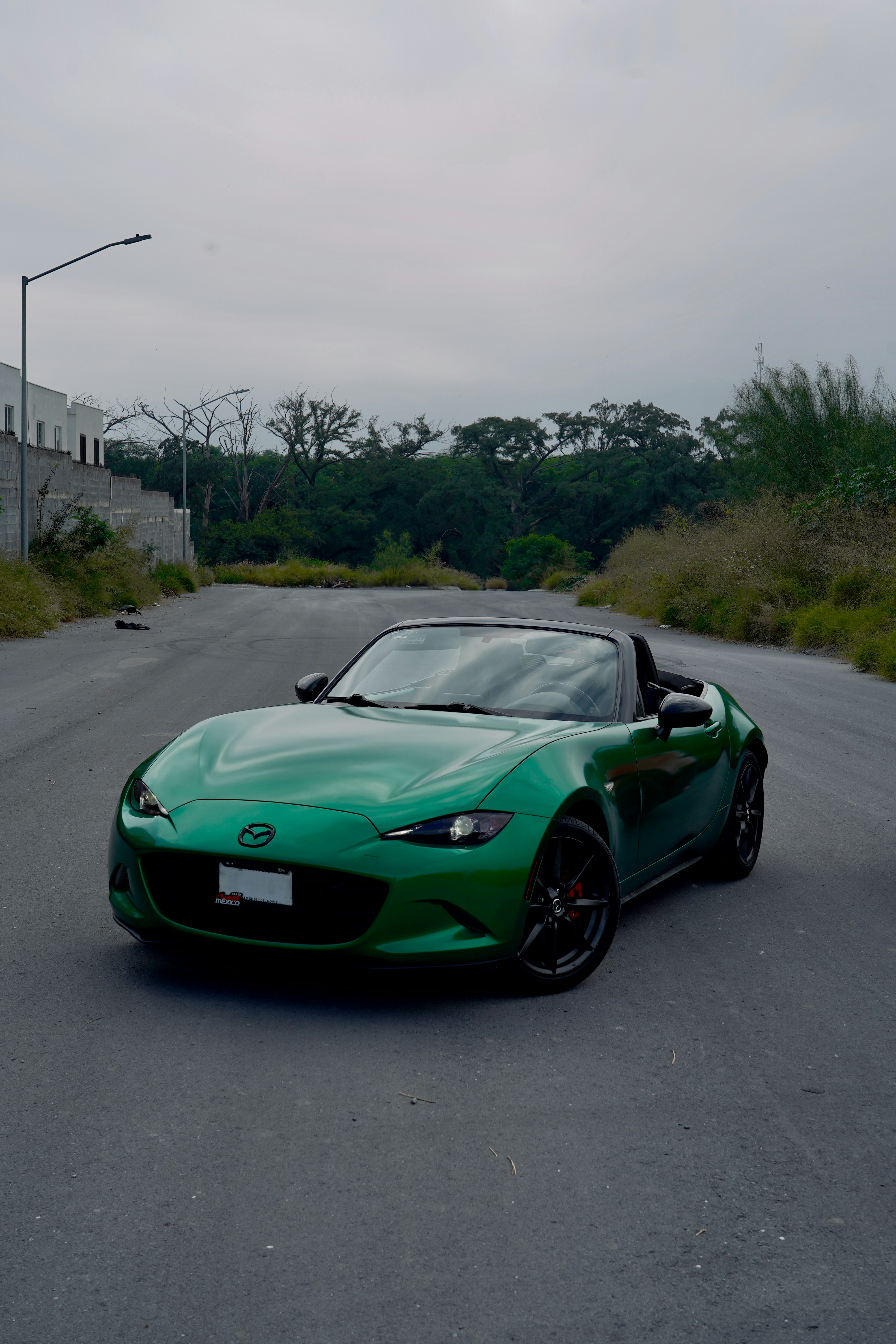 Coche deportivo descapotable verde aparcado en carretera asfaltada.