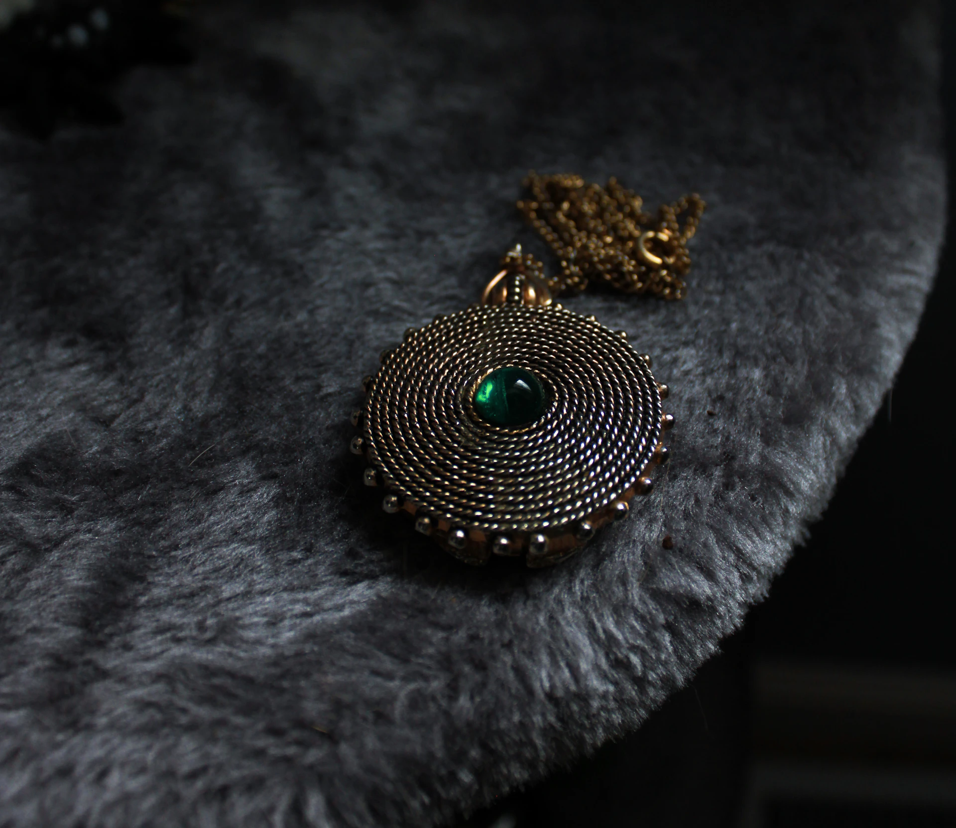 A gold pendant with a green gem rests on fur.