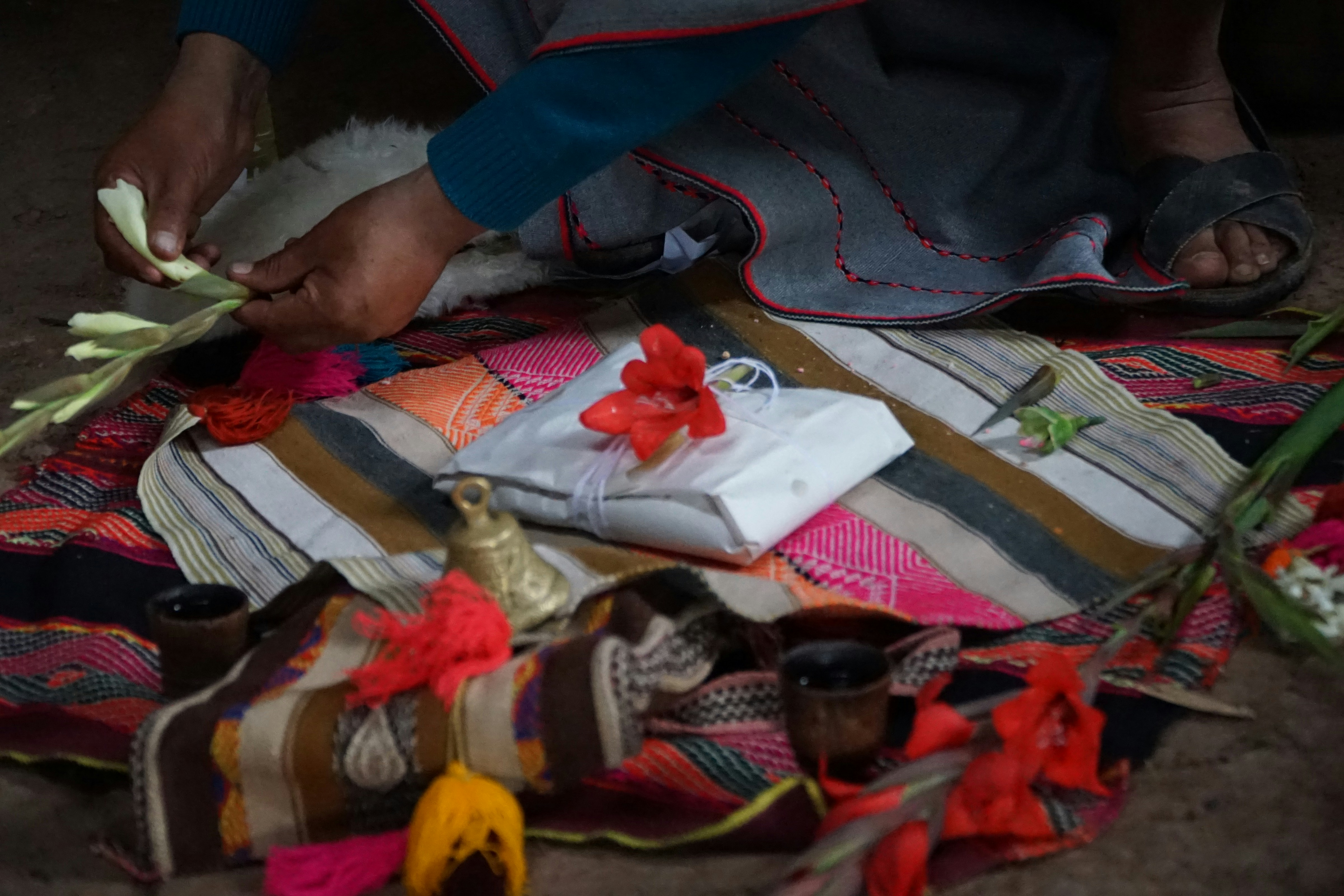 A person arranges offerings on a colorful woven cloth.