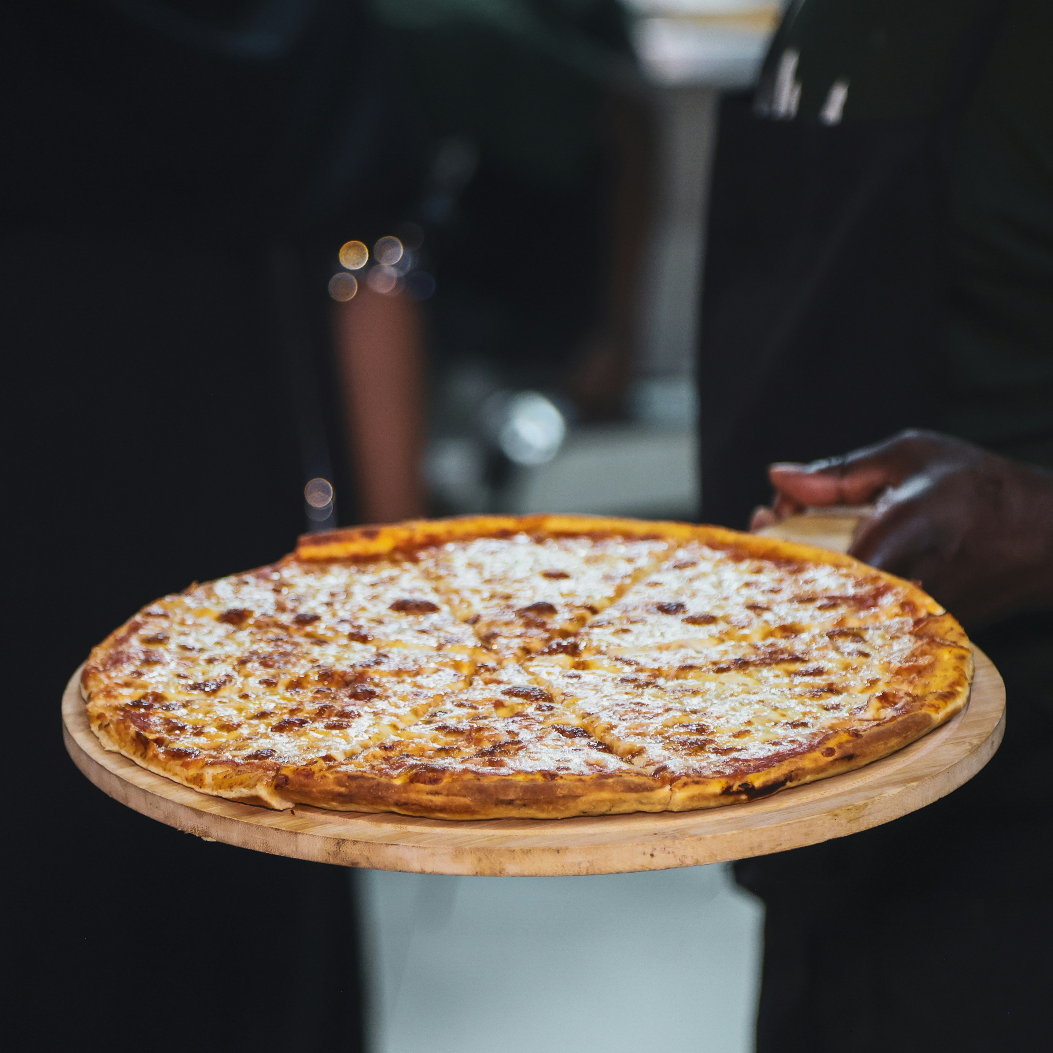 A person holding a freshly baked cheese pizza.