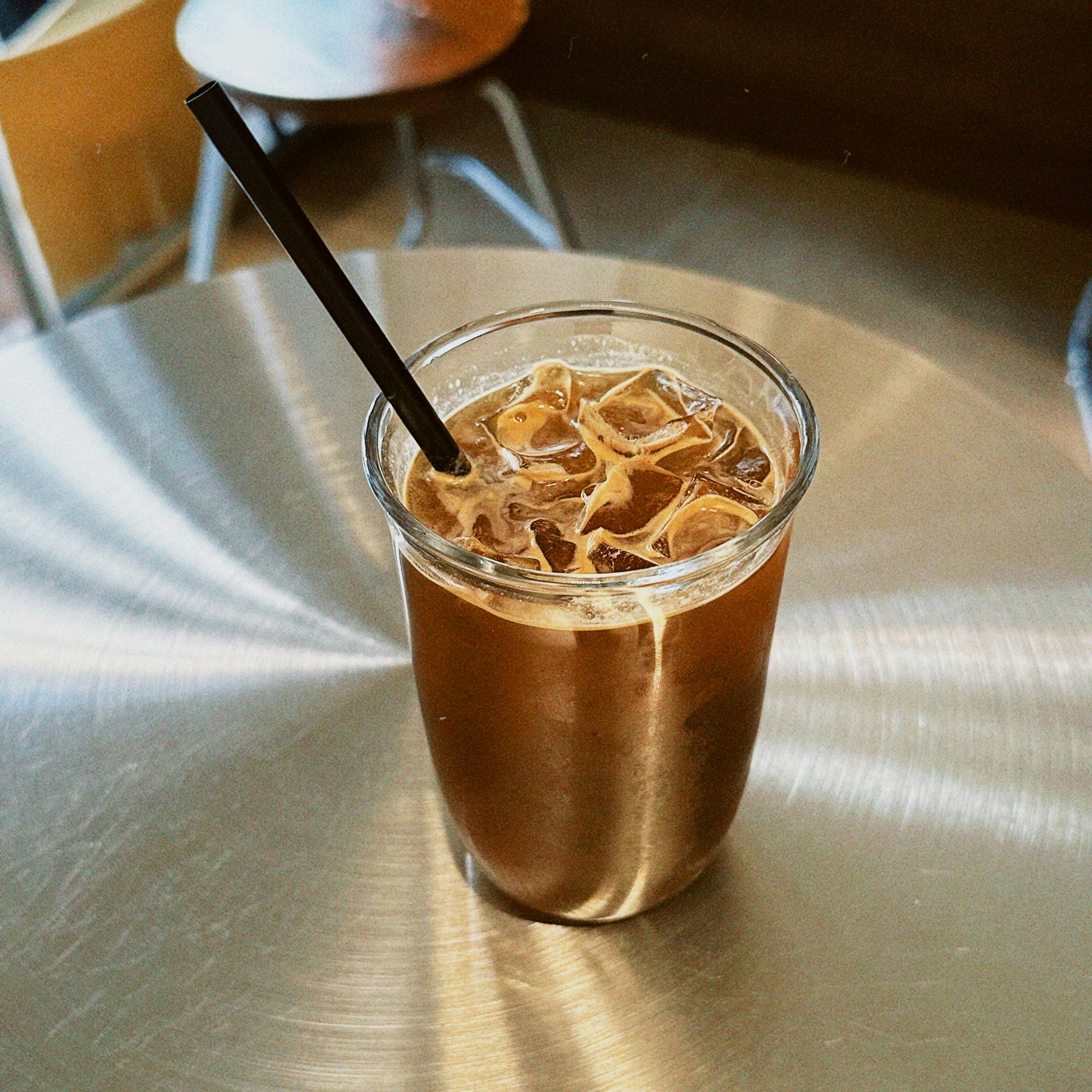 Iced coffee with a straw on a metal table.