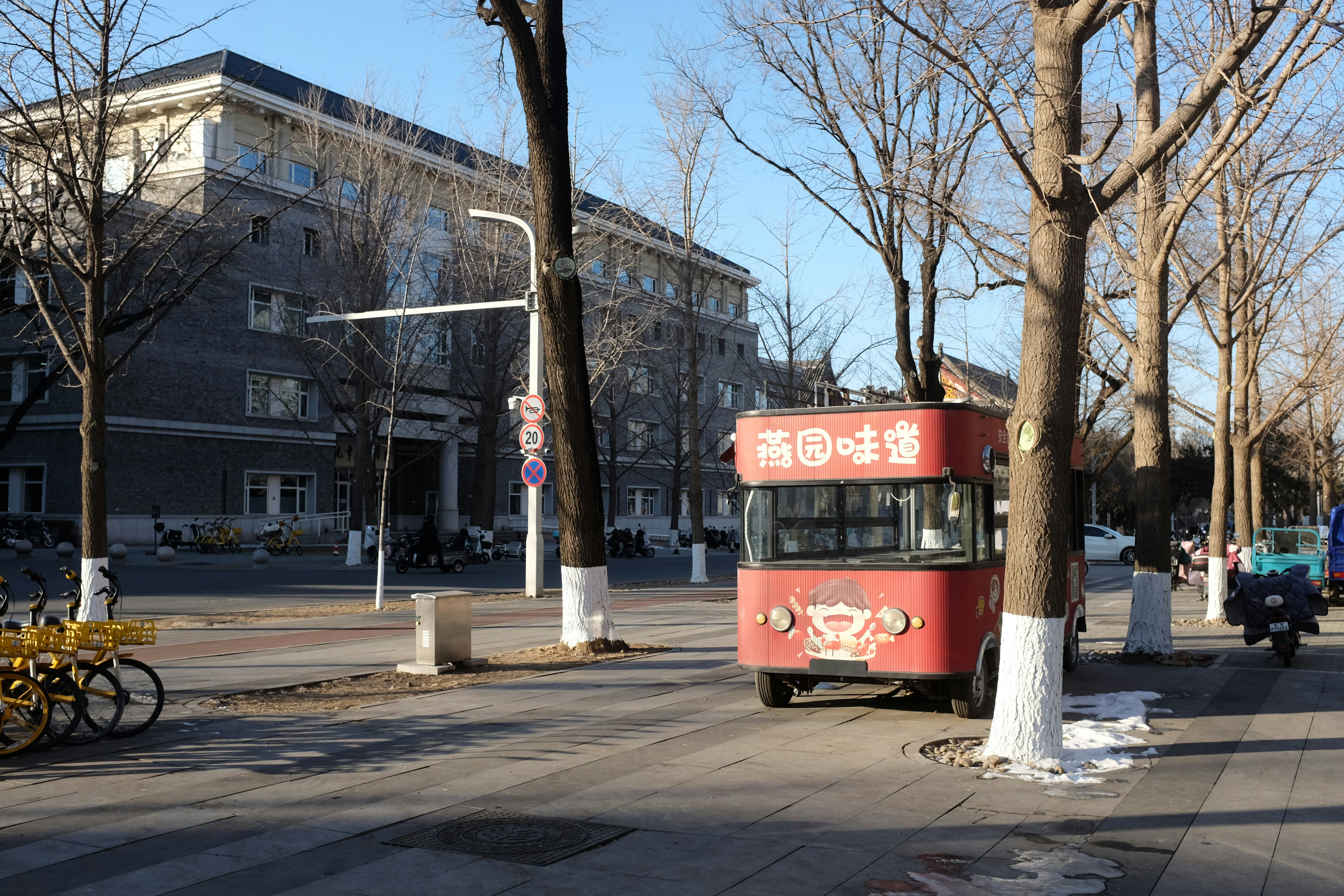 Red food cart on a street with trees and buildings.