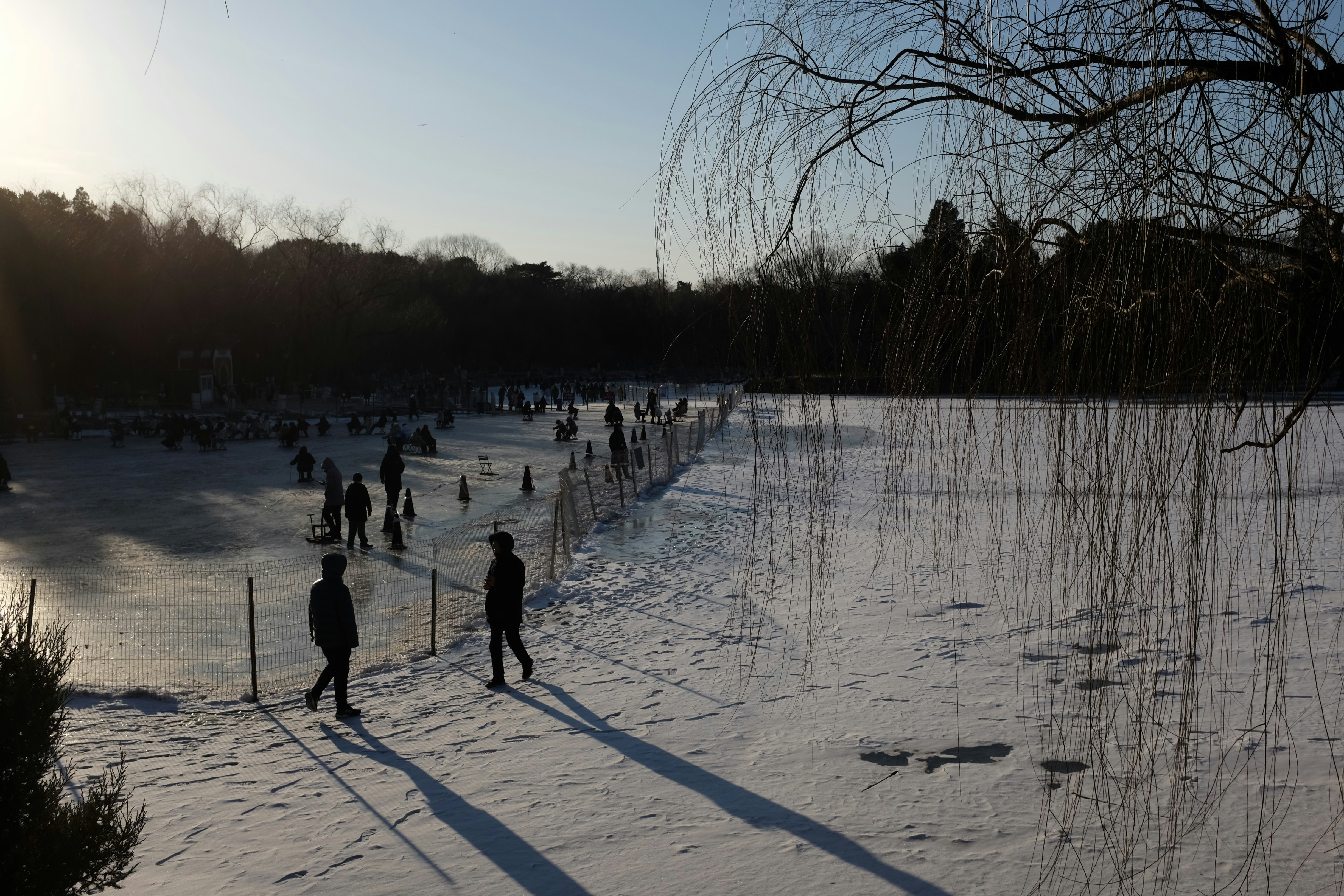 People walking on a snow-covered path near a frozen lake.