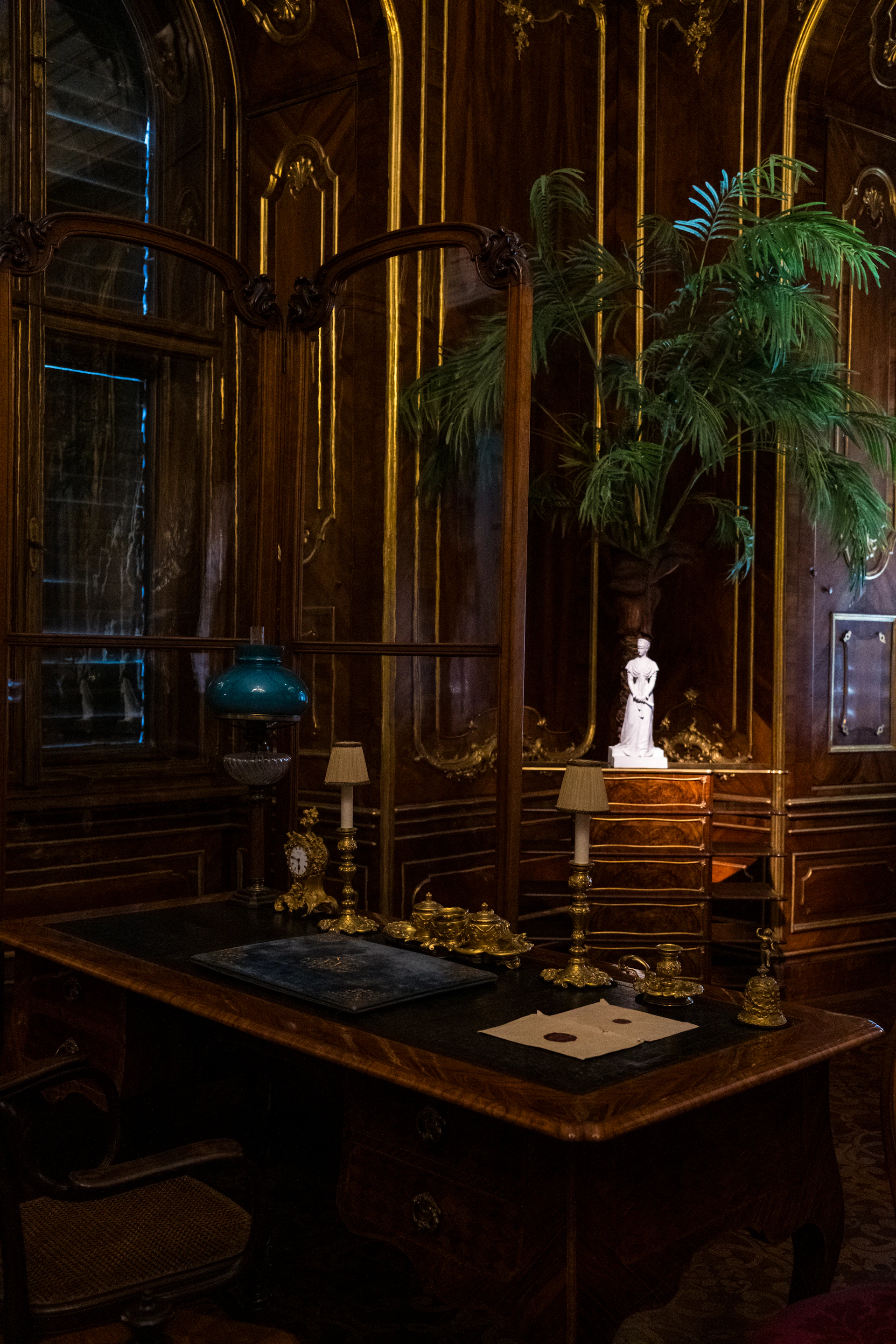 Ornate wooden office with antique desk and lamp.