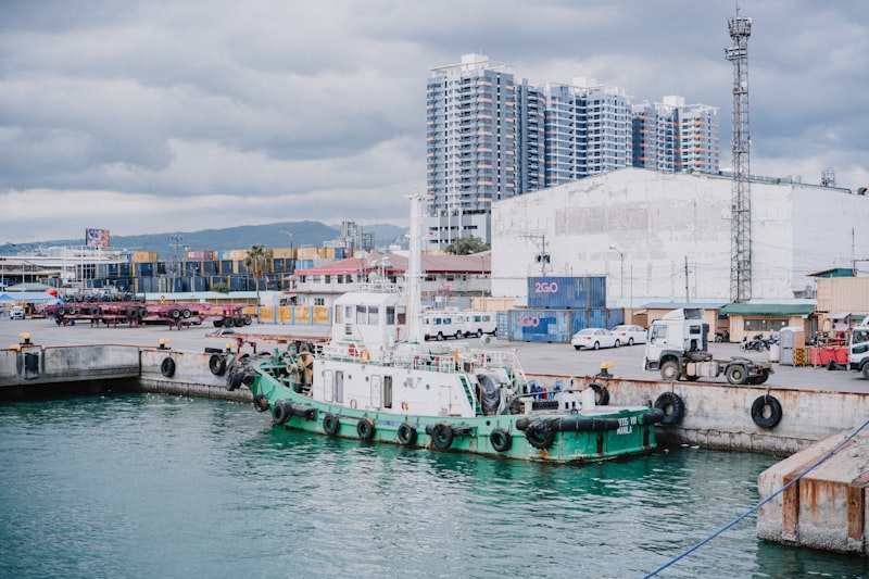 A tugboat docked in a busy harbour with cargo infrastructure behind