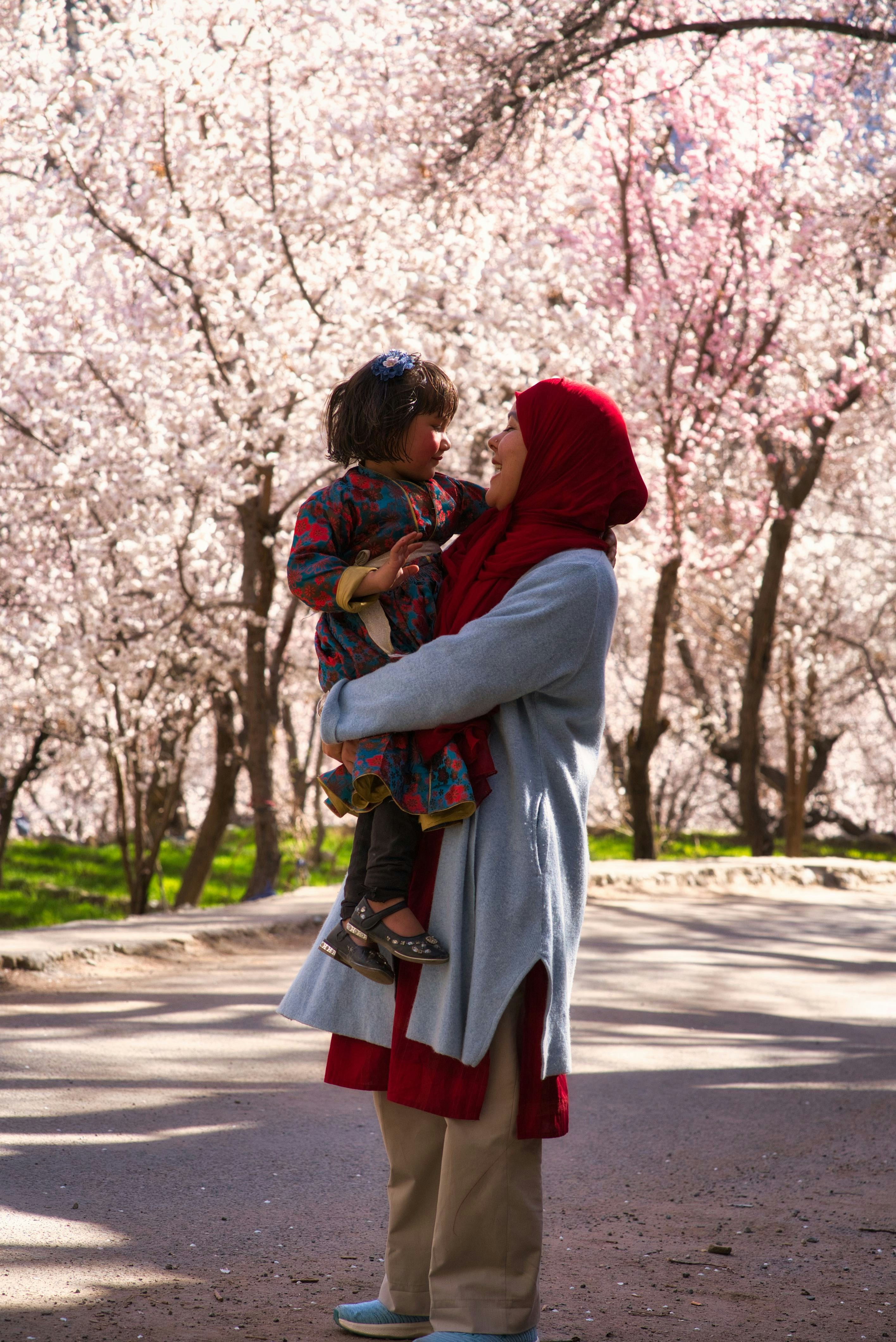 Ibu menggendong anak di bawah pohon sakura yang mekar