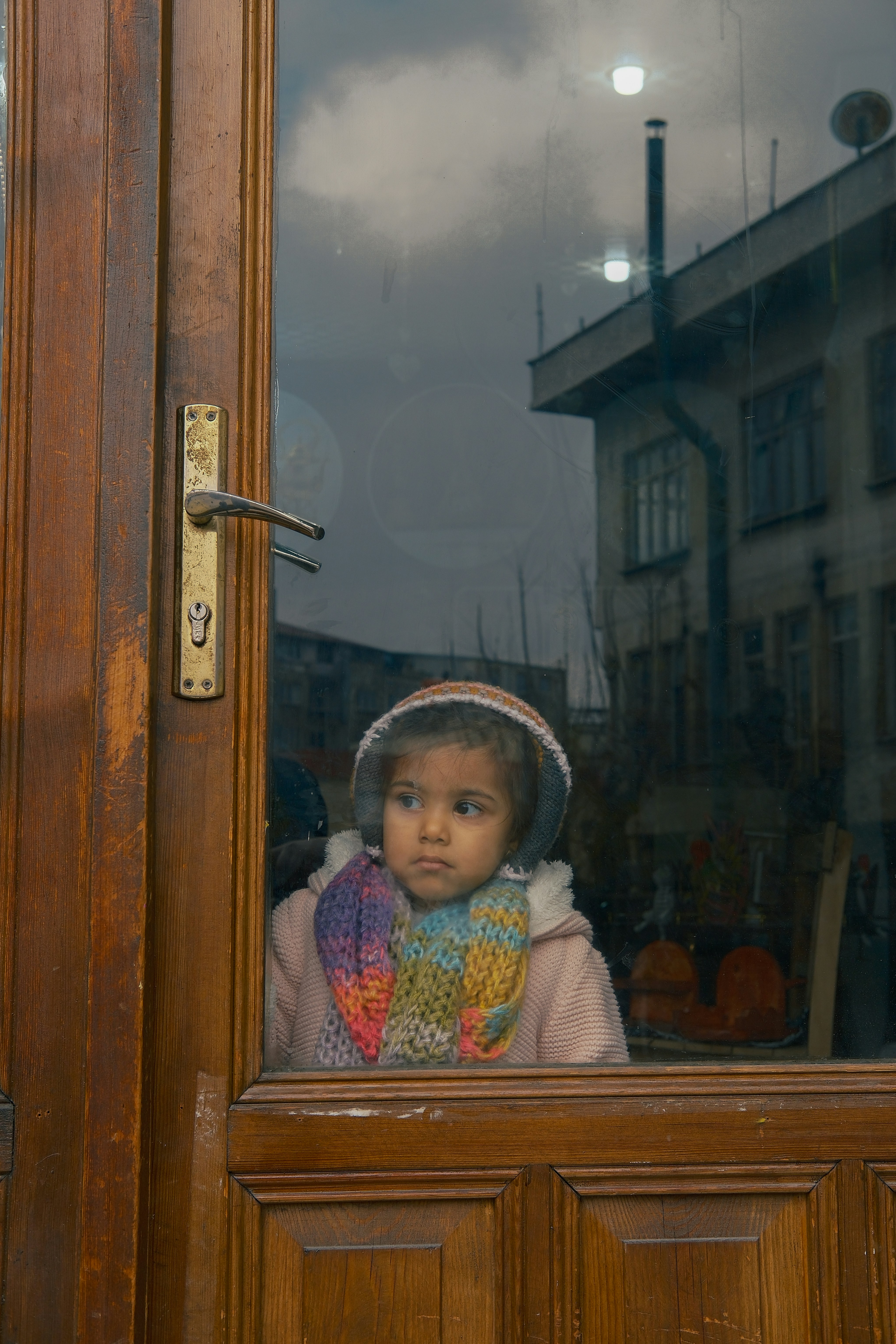 Young girl looking out a glass door