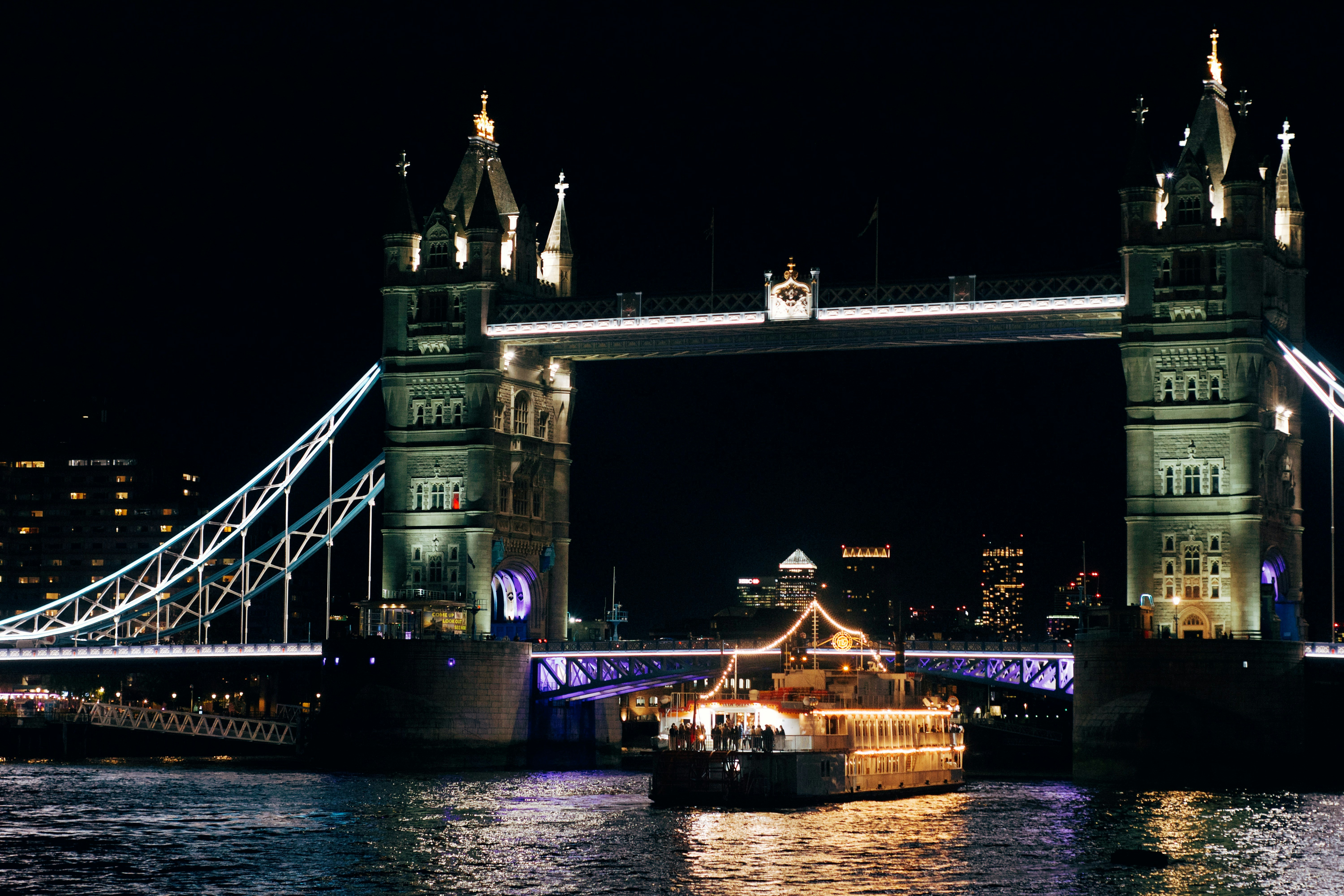 Puente de la torre iluminado por la noche con barco en el río.
