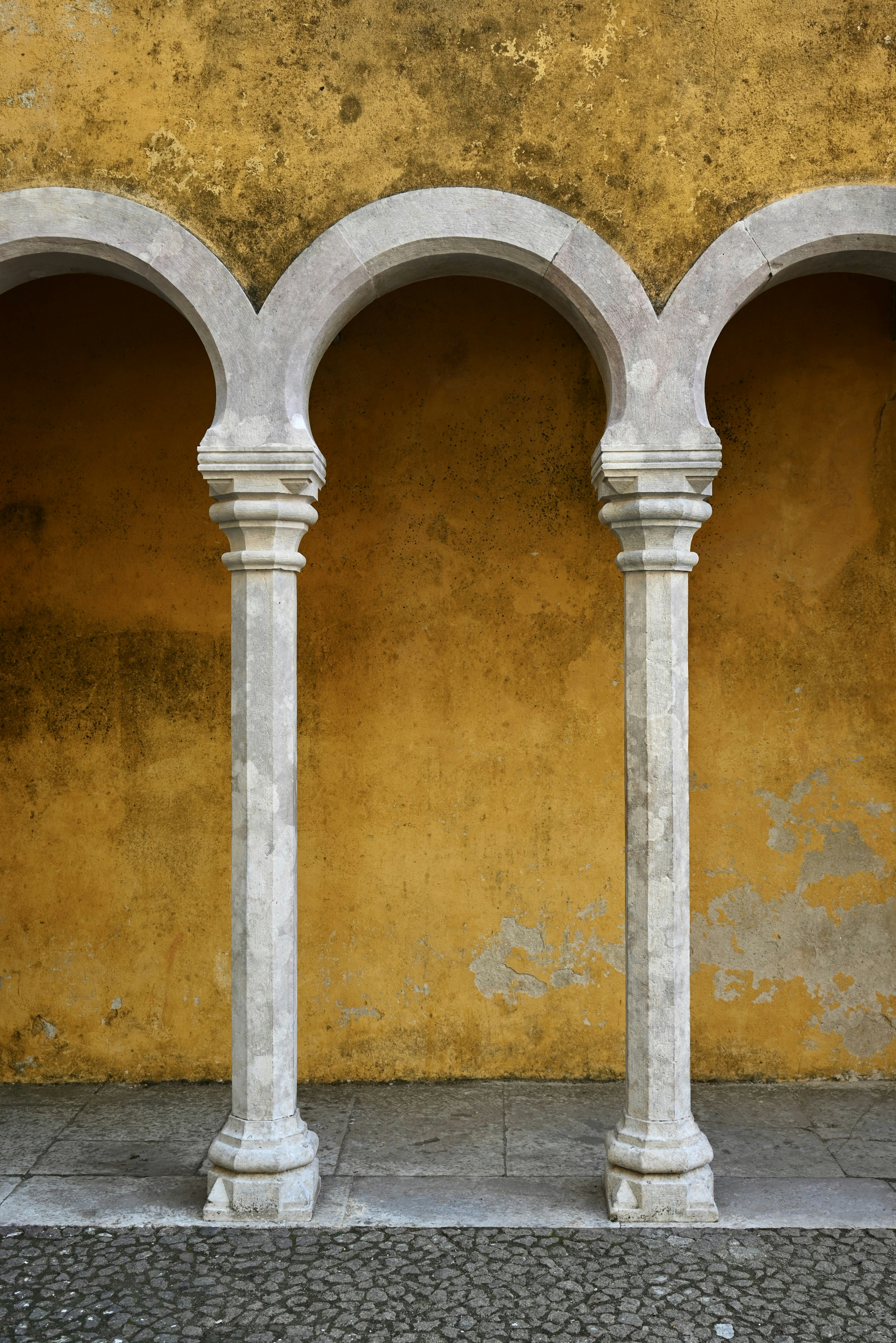 Three arched columns against a textured yellow wall.