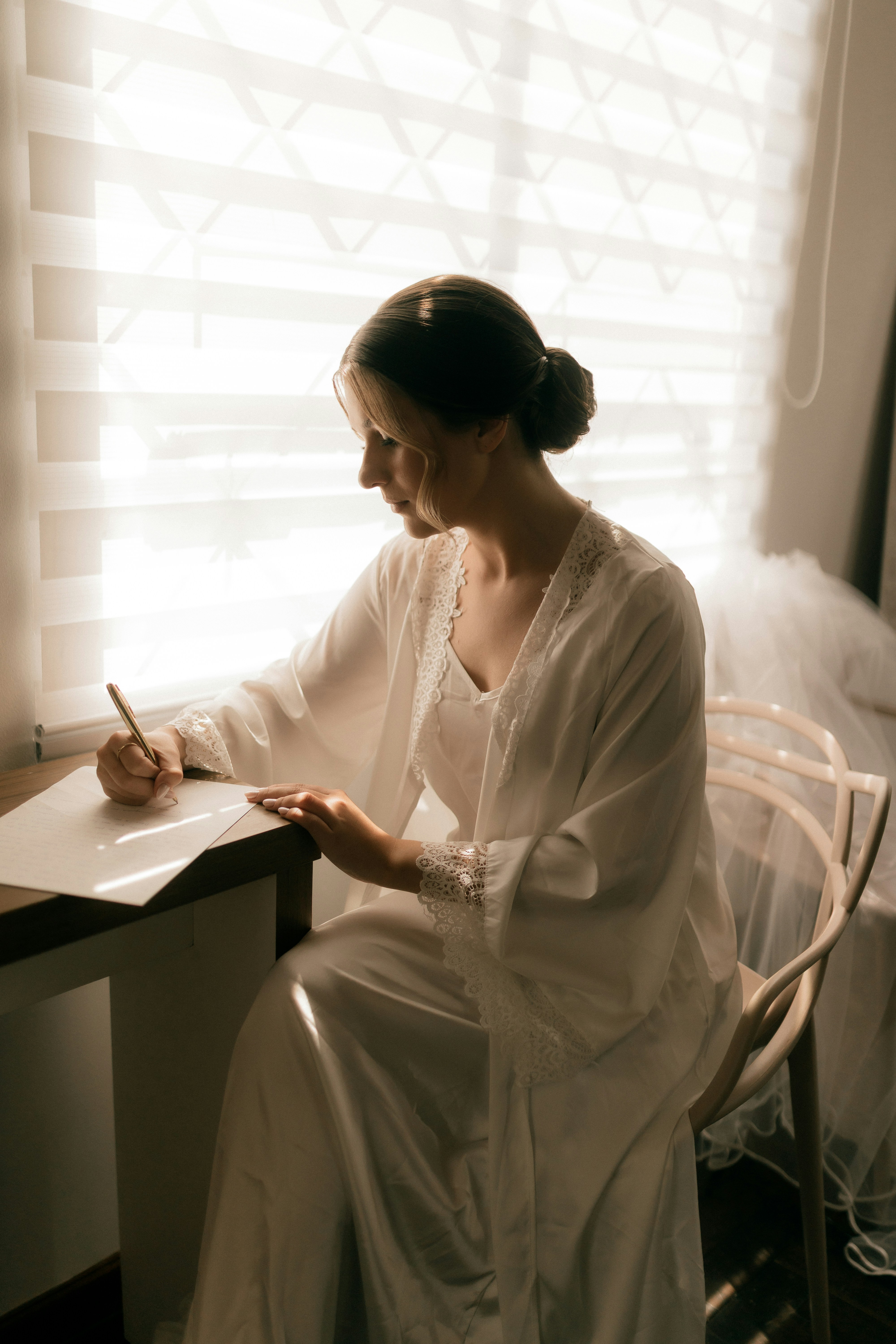Donna in abito bianco che scrive alla scrivania vicino alla finestra
