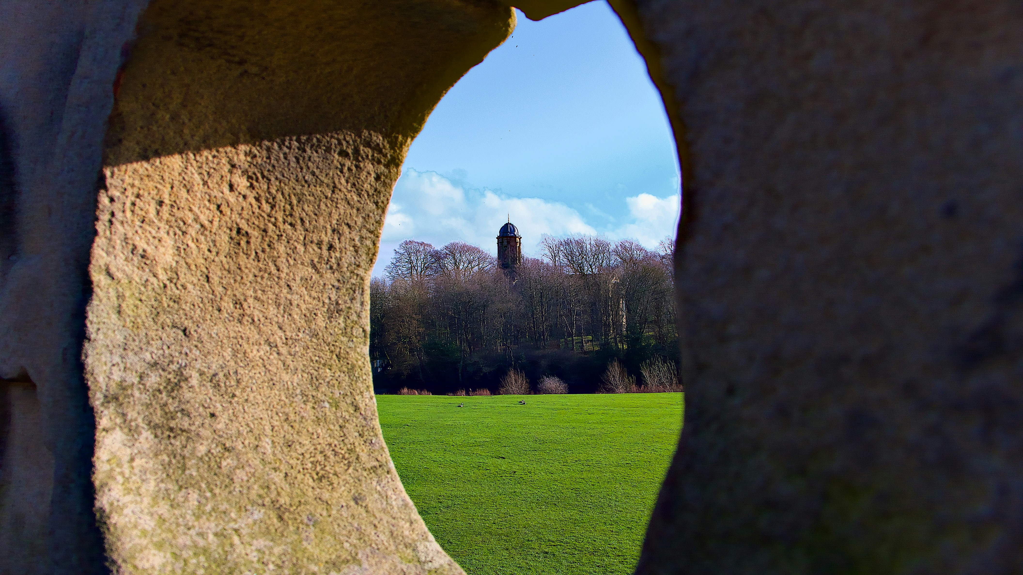 View through stone archway of trees and field.