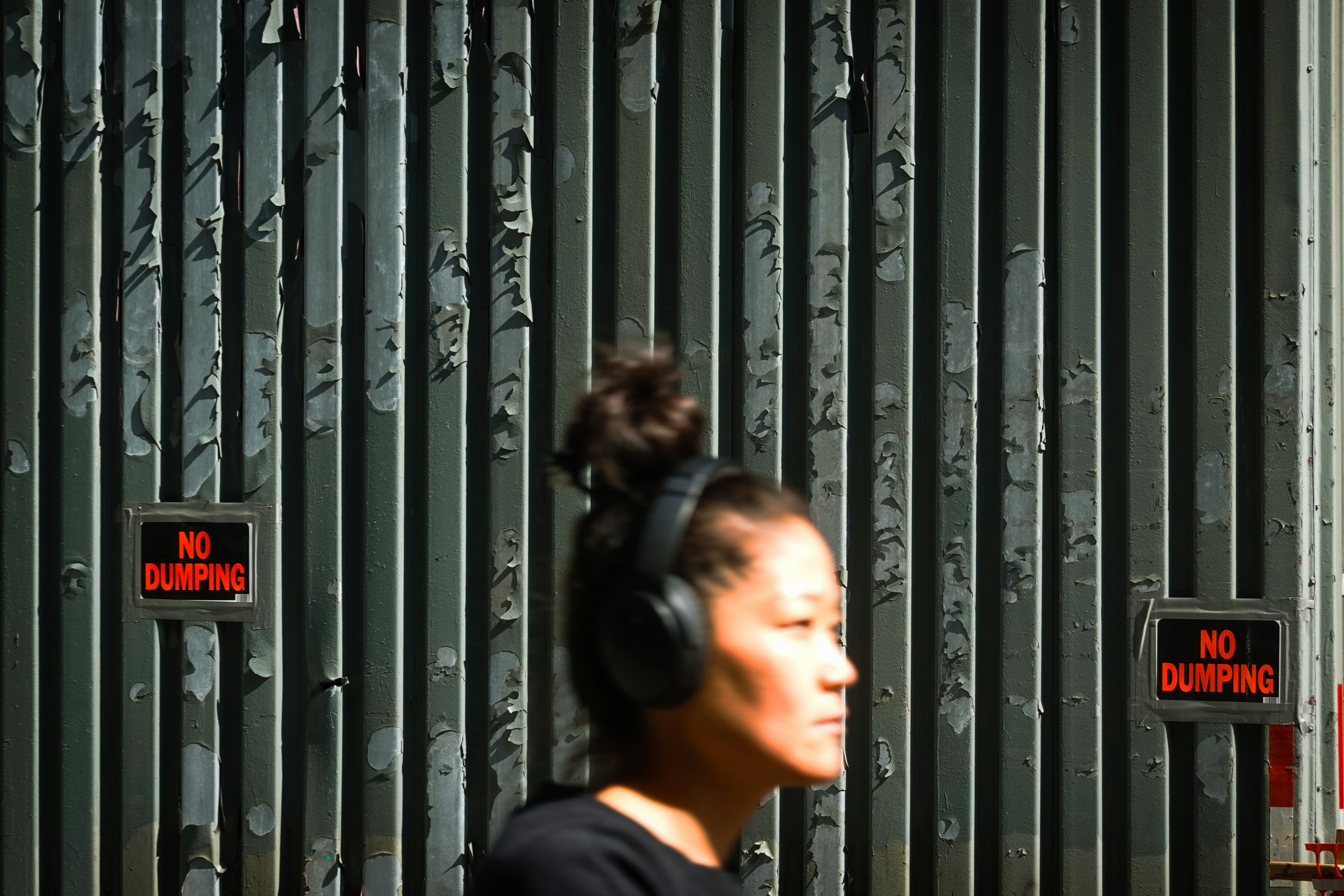Woman with headphones walks past a metal gate