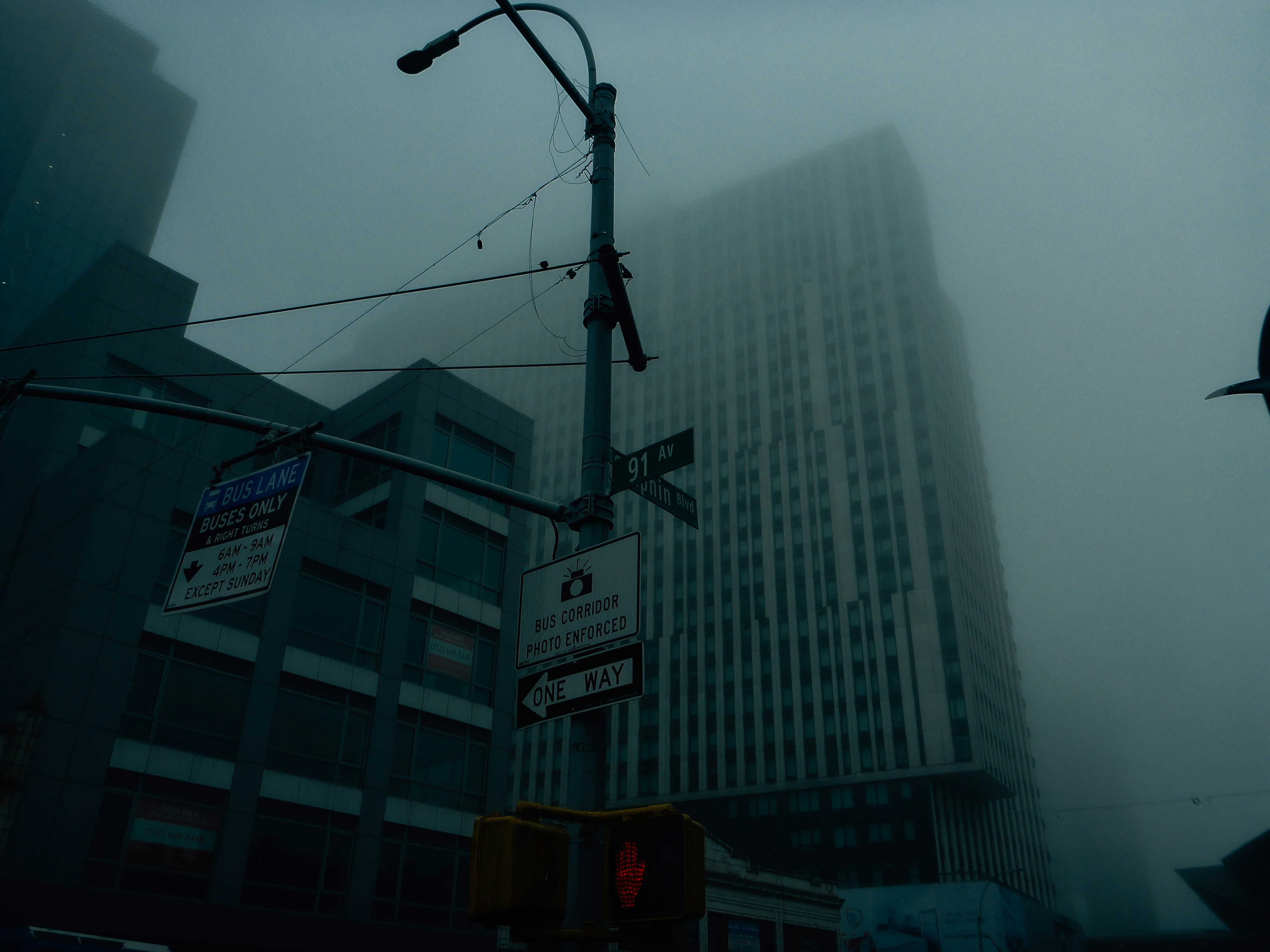Tall building shrouded in fog on a city street.