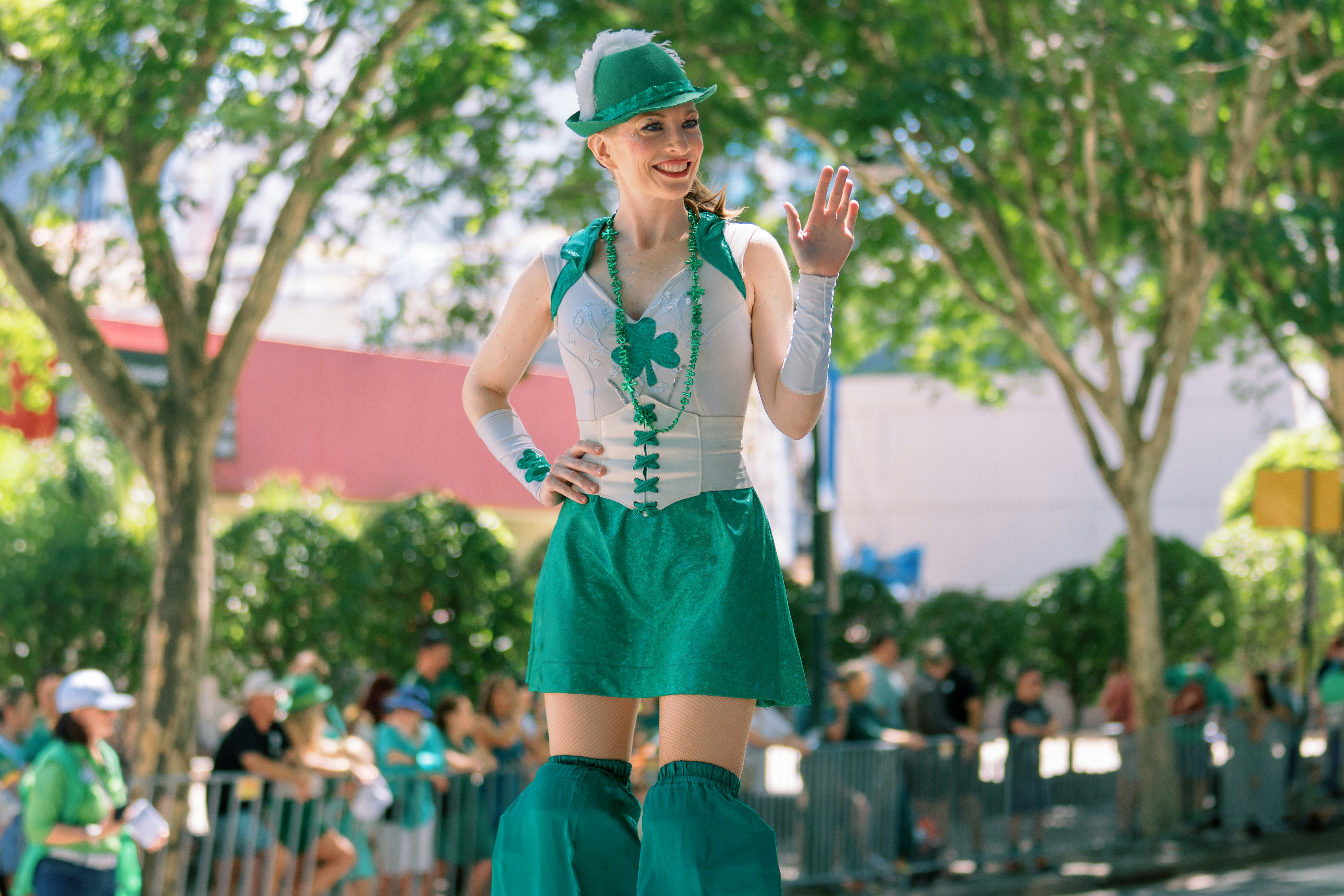 Woman in green costume on stilts waving at parade