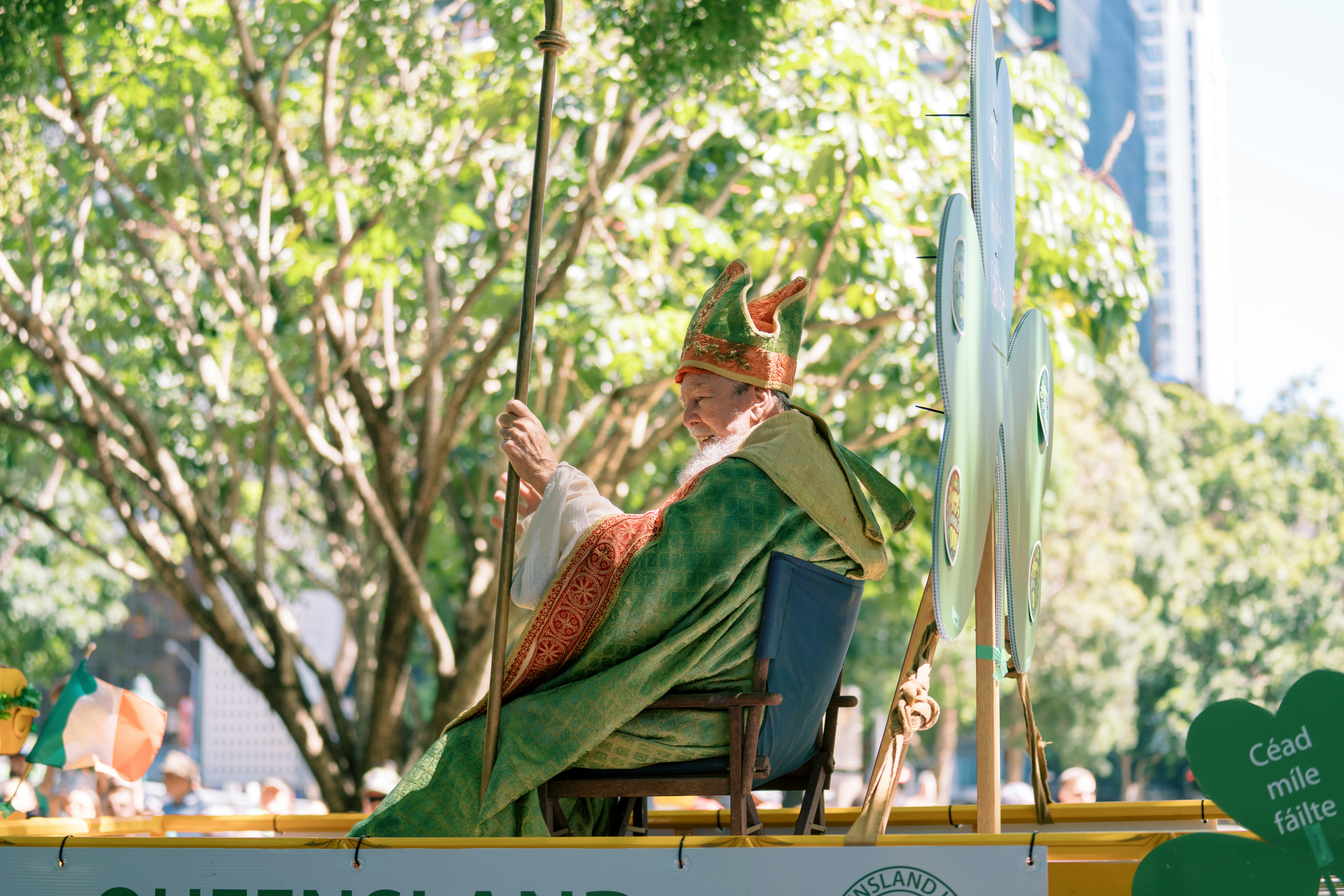 Man in costume sits on a chair holding staff.