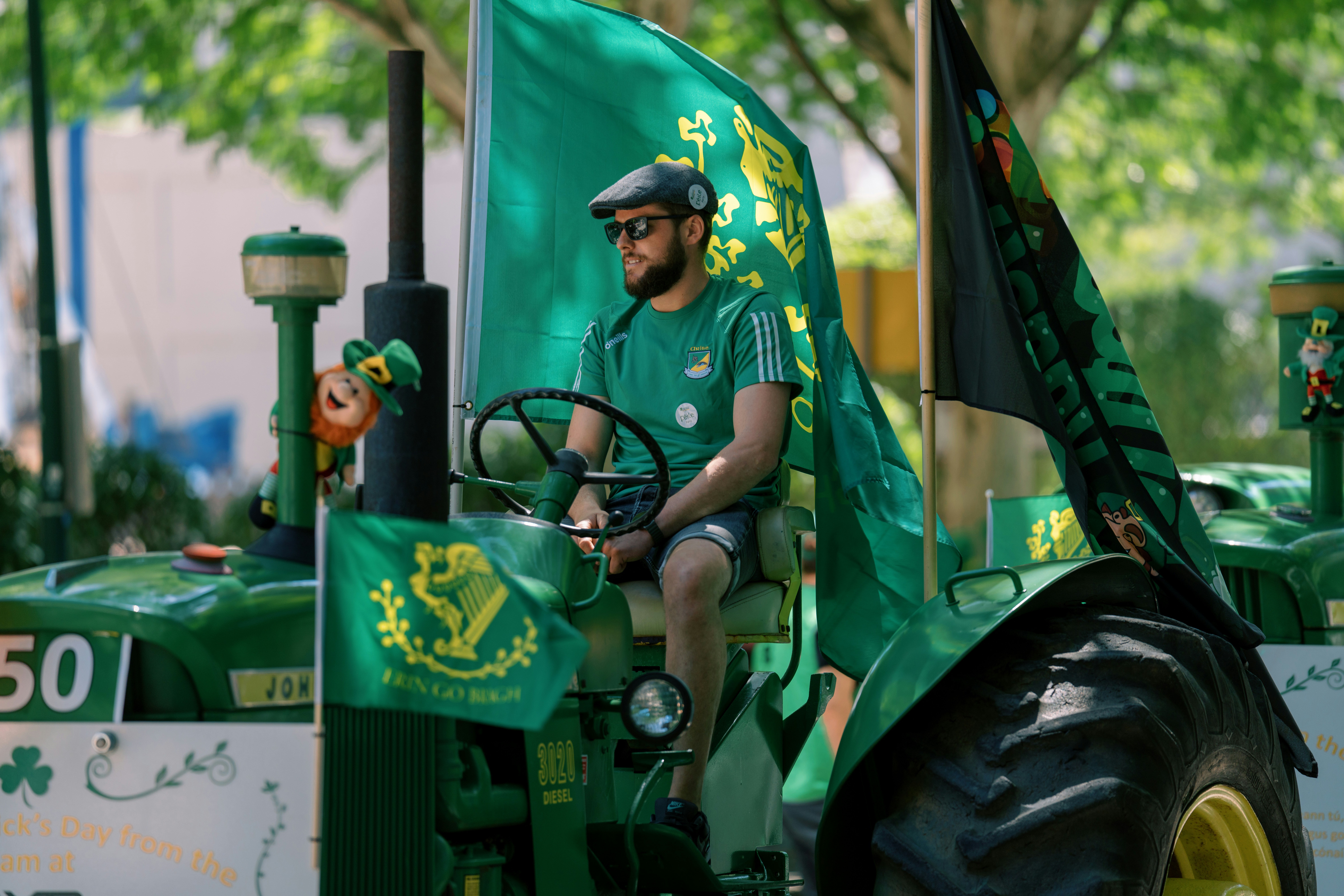 Man in green shirt driving decorated tractor with flags